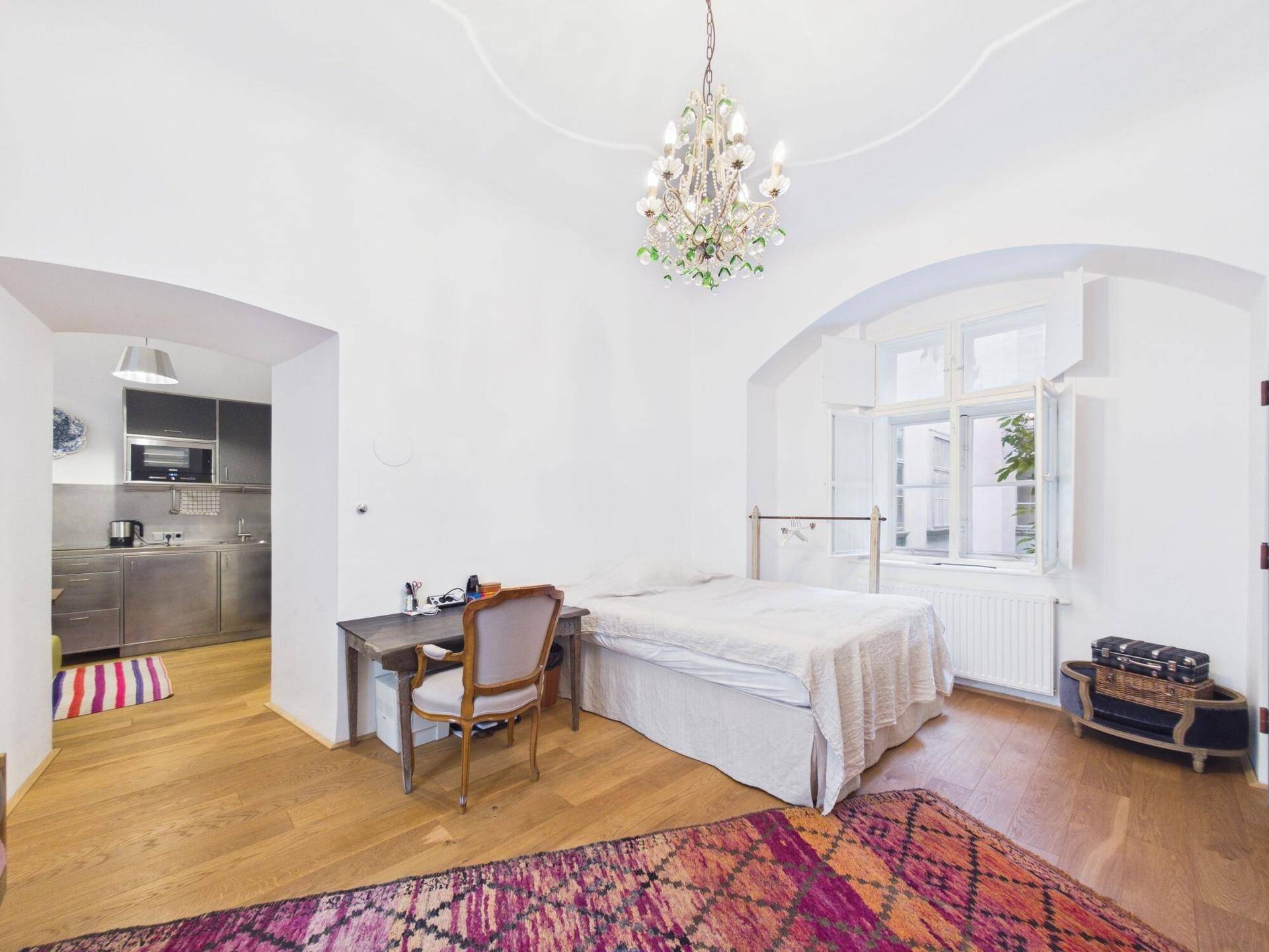 Schlafzimmer mit Holzboden und Blick auf eine angrenzende, moderne Küchenzeile.