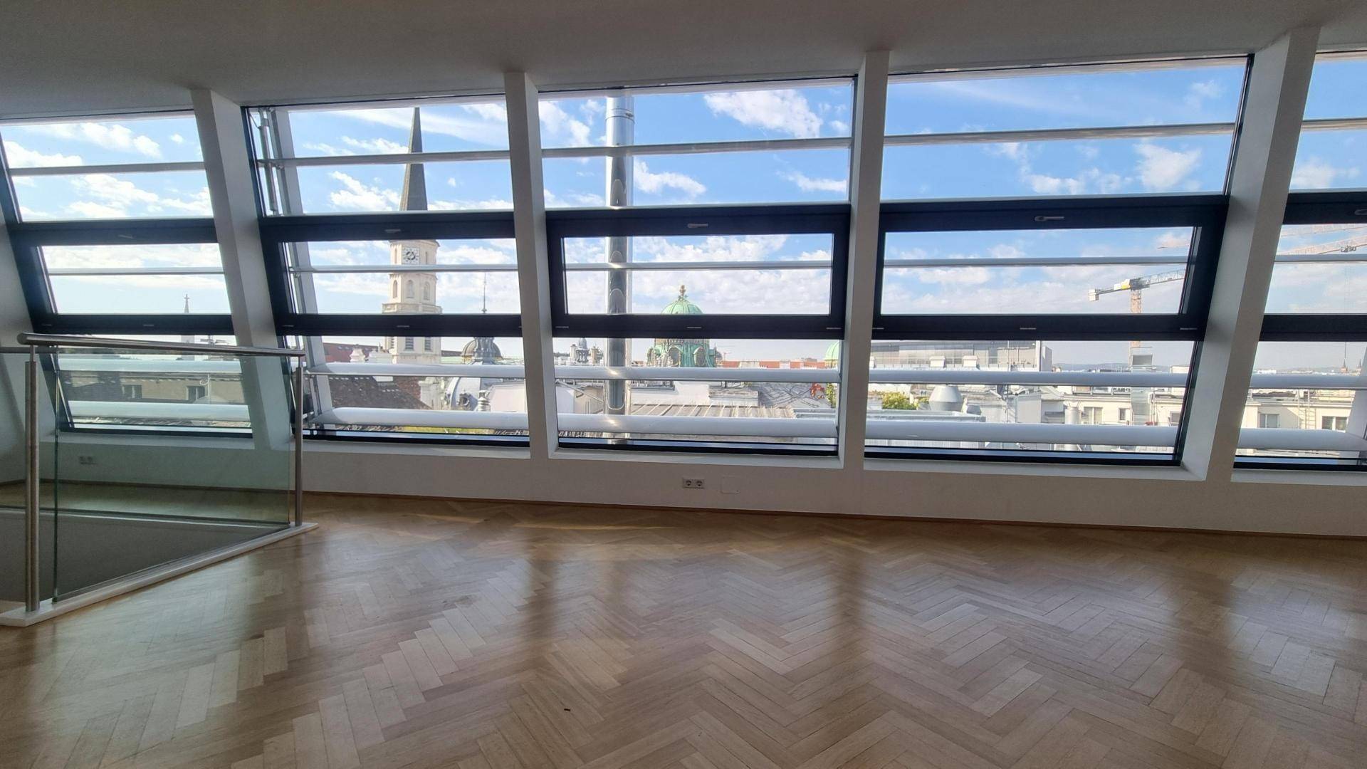 Heller Wohnraum mit Fischgrätparkett und großen, schrägen Fenstern mit Stadtblick.