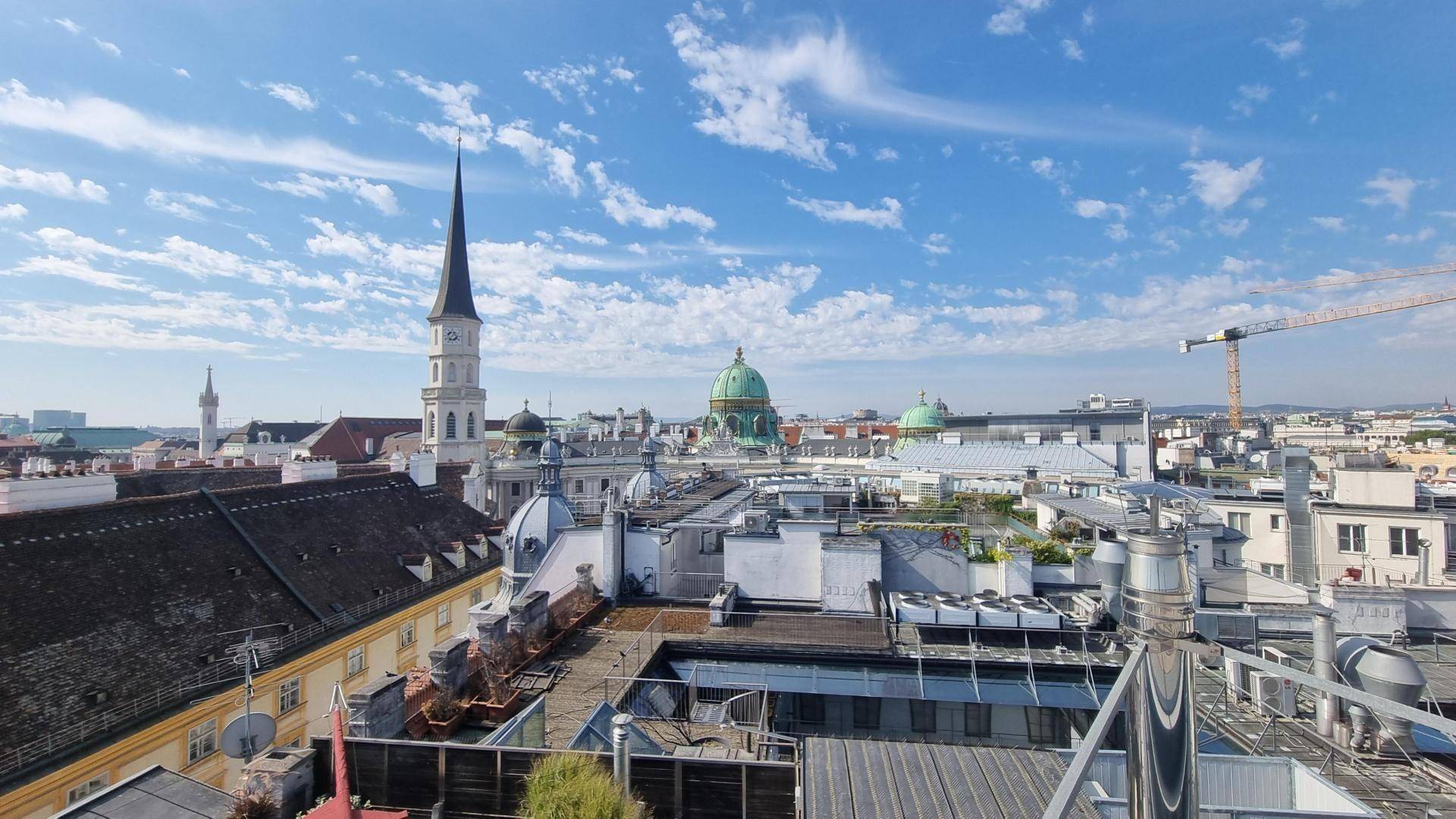 Panoramablick über die Dächer der Stadt mit historischen Gebäuden und einem Baukran am Horizont.
