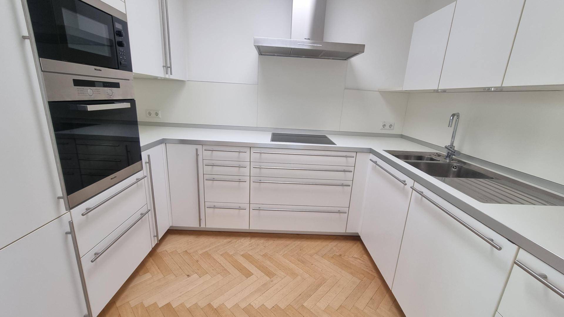 Moderne Einbauküche mit weißen Fronten, integrierten Geräten und hellem Fischgrätparkett.