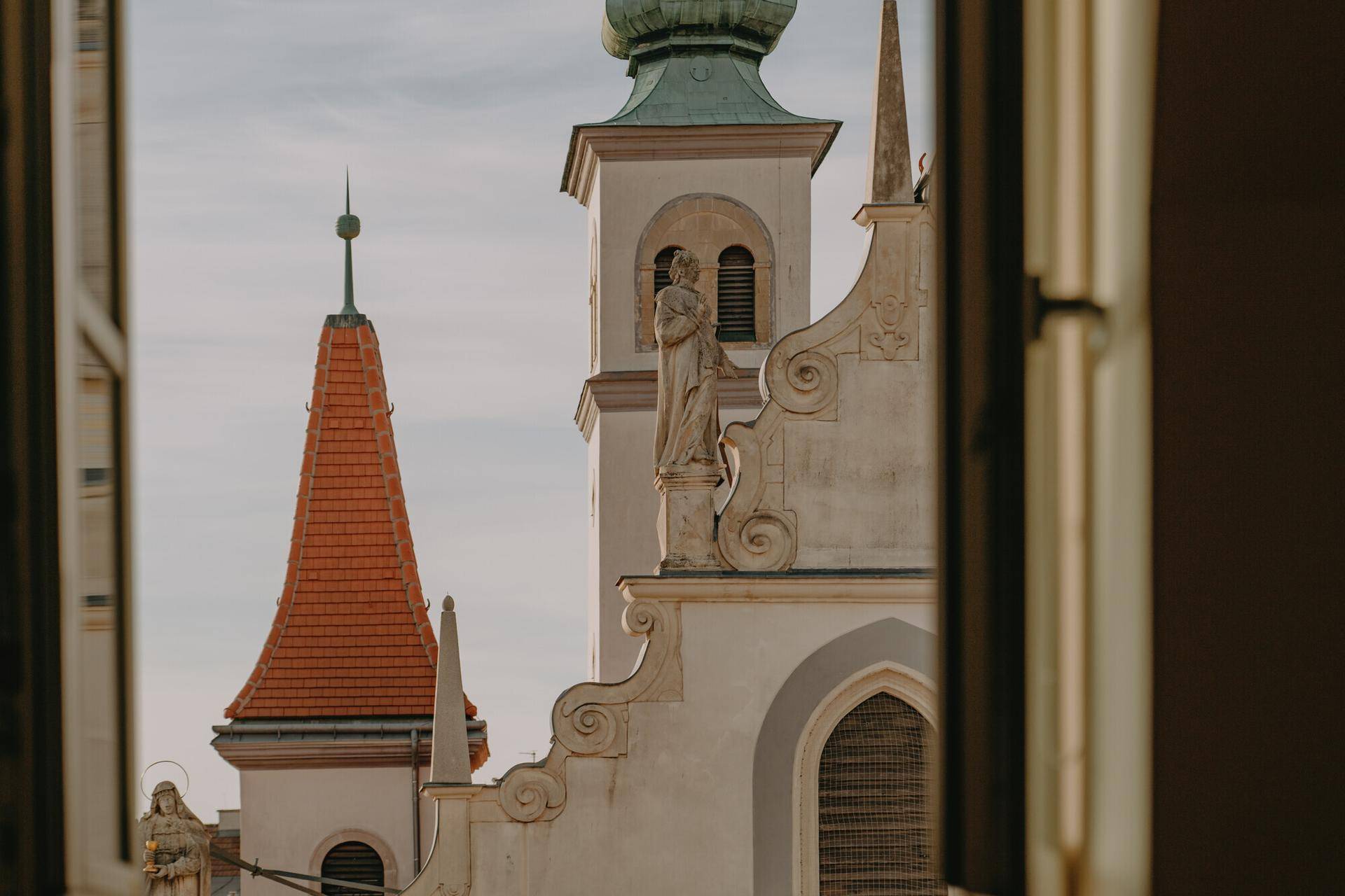 Historische Kirchtürme mit grünen Kuppeln und barocken Verzierungen, durch ein Fenster gesehen.