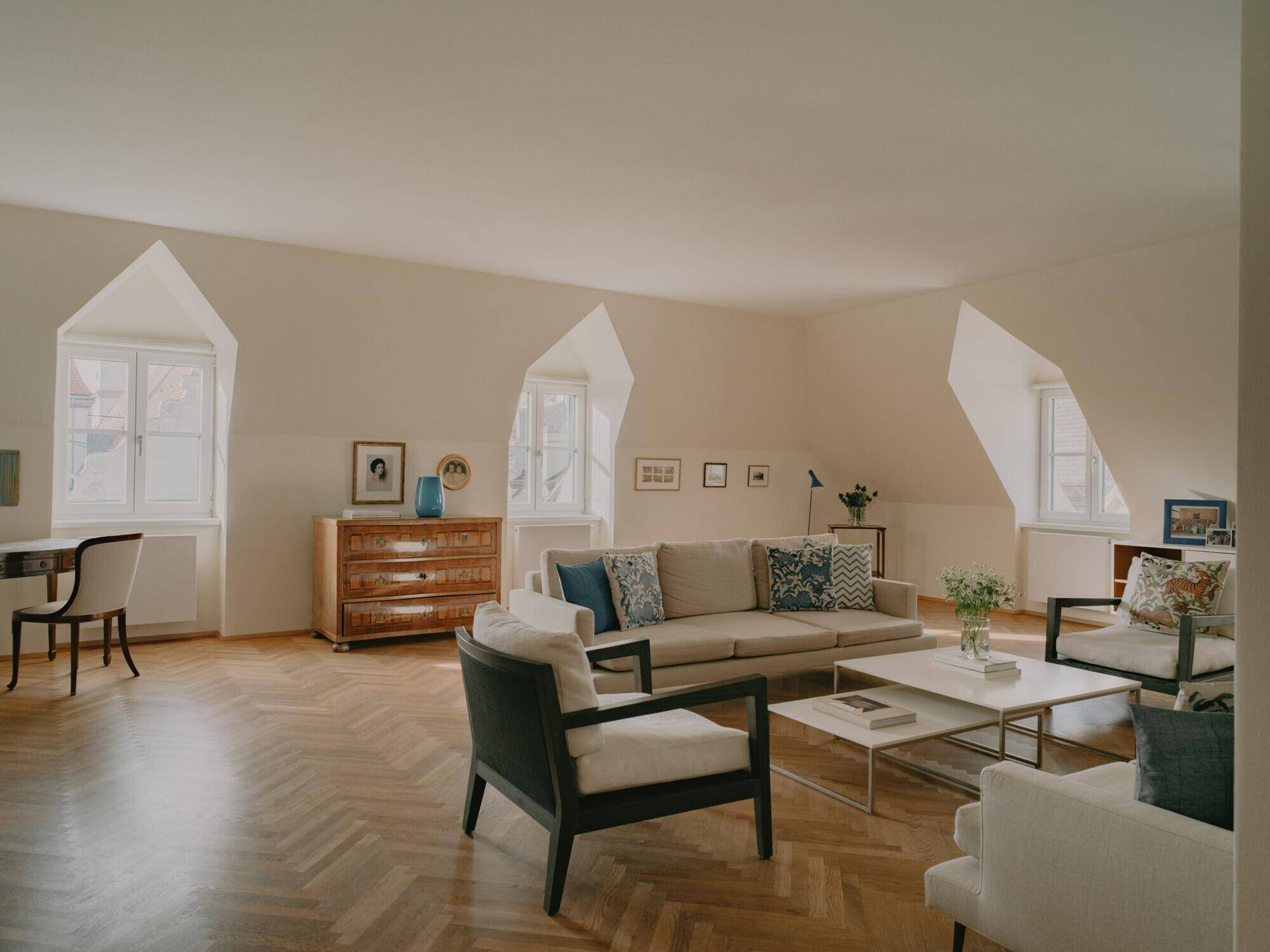 Helles Wohnzimmer im Dachgeschoss mit schrägen Wänden, Fischgrätparkett und gemütlicher Sitzecke.