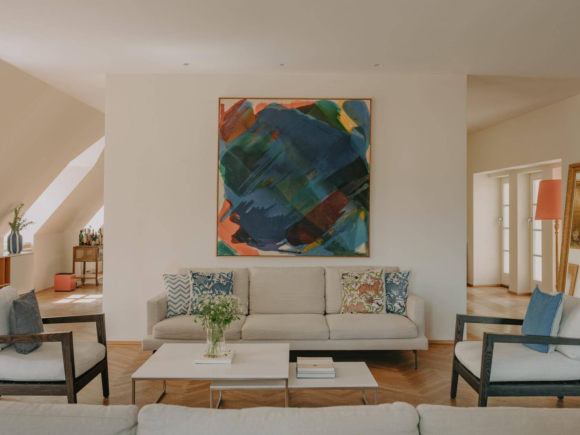Gemütliches Wohnzimmer mit beigem Sofa, farbenfrohem Kunstwerk und Fischgrätparkett.