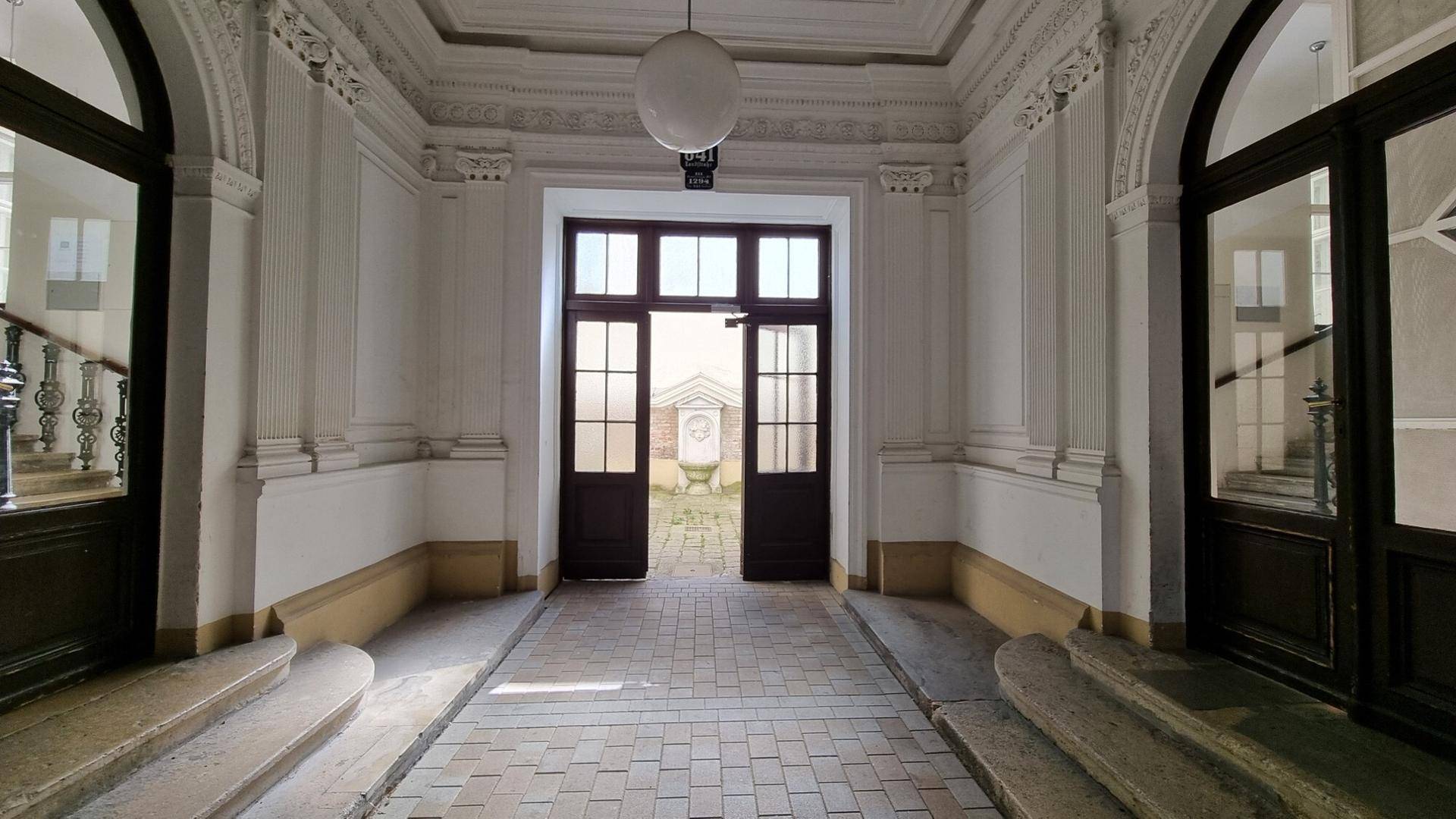 Repräsentativer Eingangsbereich mit hohen Decken, Stuckverzierungen und Zugang zum Innenhof.