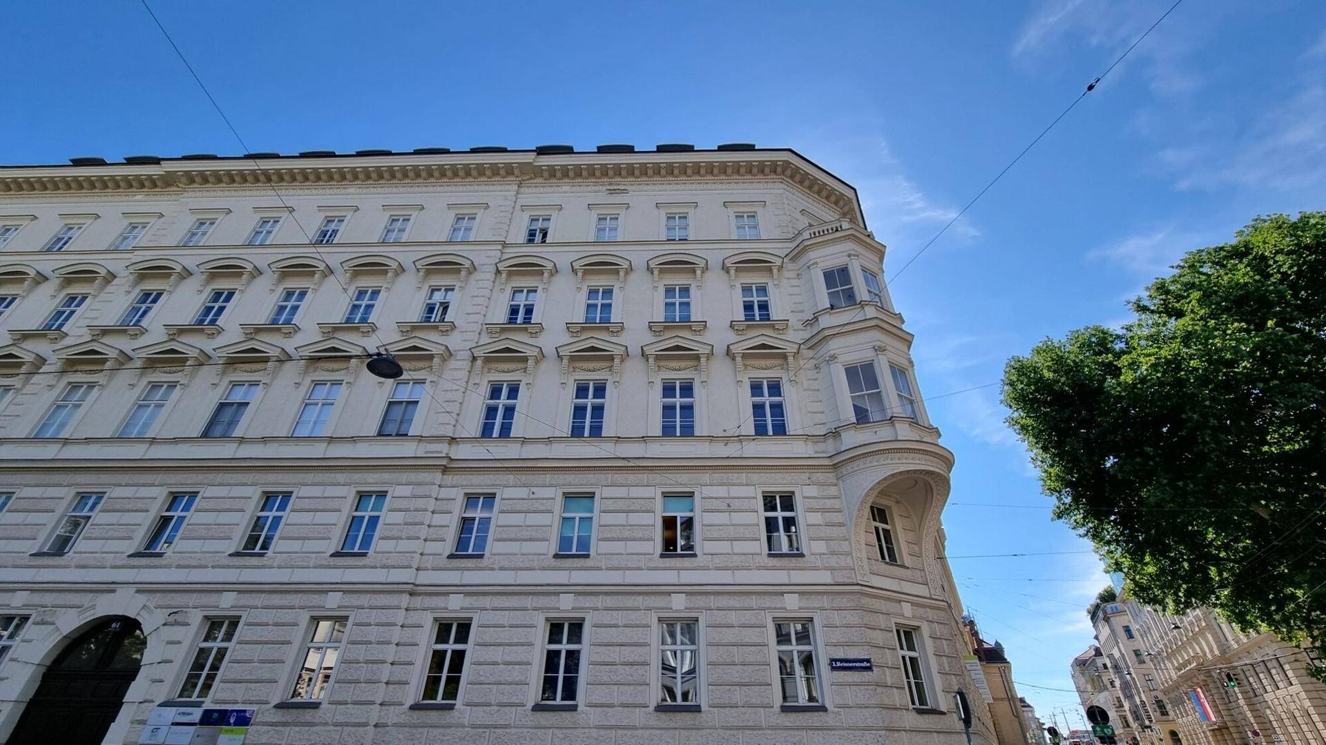 Historisches Eckgebäude mit klassischer Architektur und vielen Fenstern unter blauem Himmel.