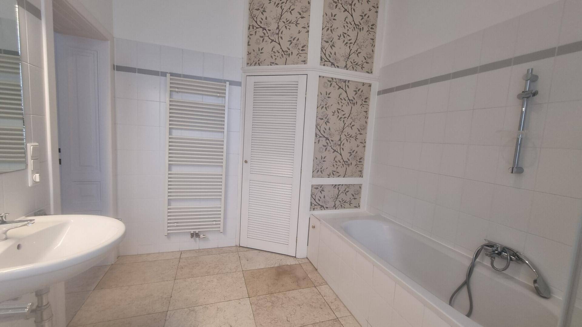 Badezimmer mit Badewanne, Waschbecken, beheiztem Handtuchhalter und dekorativer Tapete.