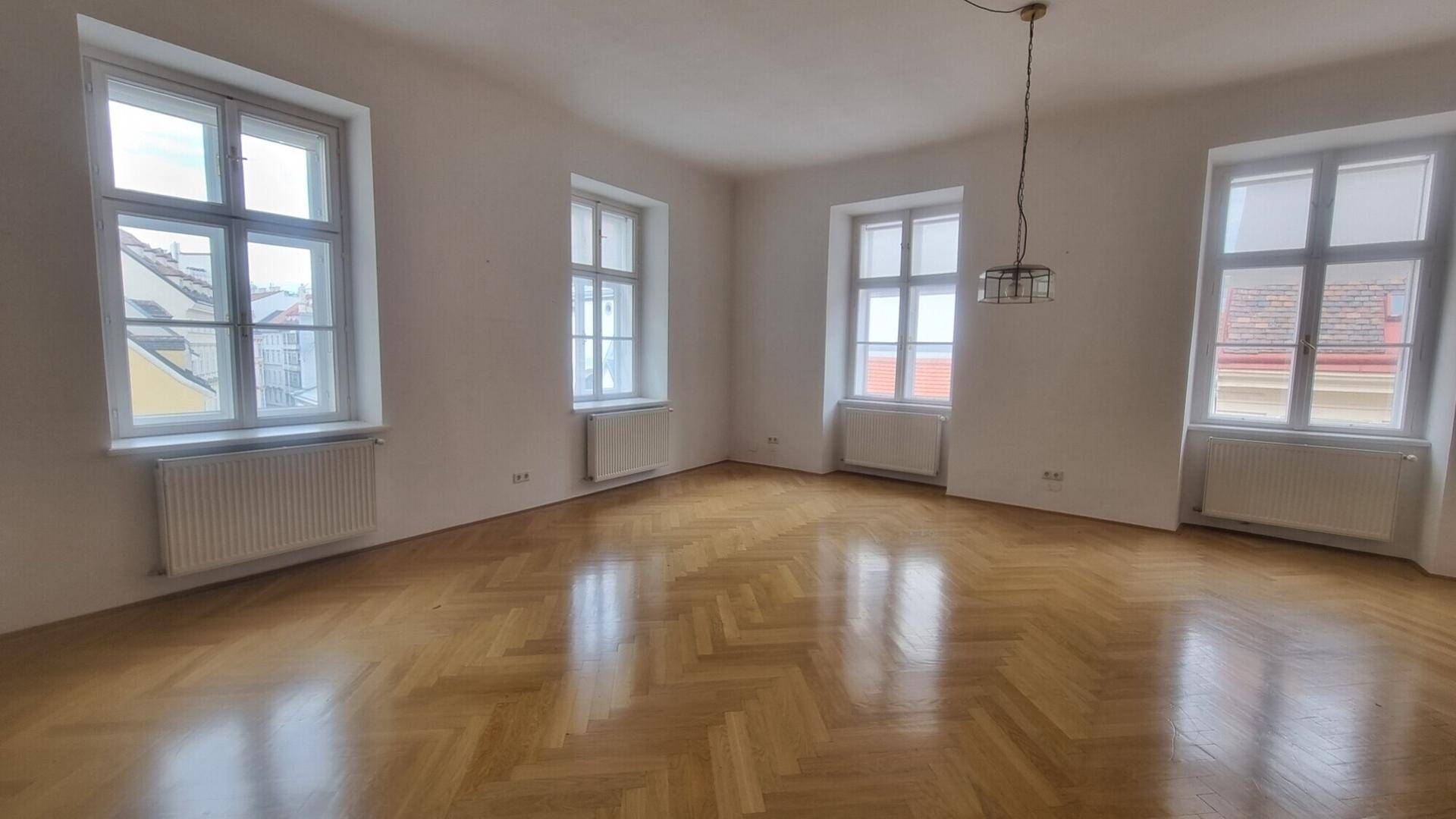 Geräumiger Raum mit klassischem Fischgrätparkett und vielen Fenstern für viel Tageslicht.