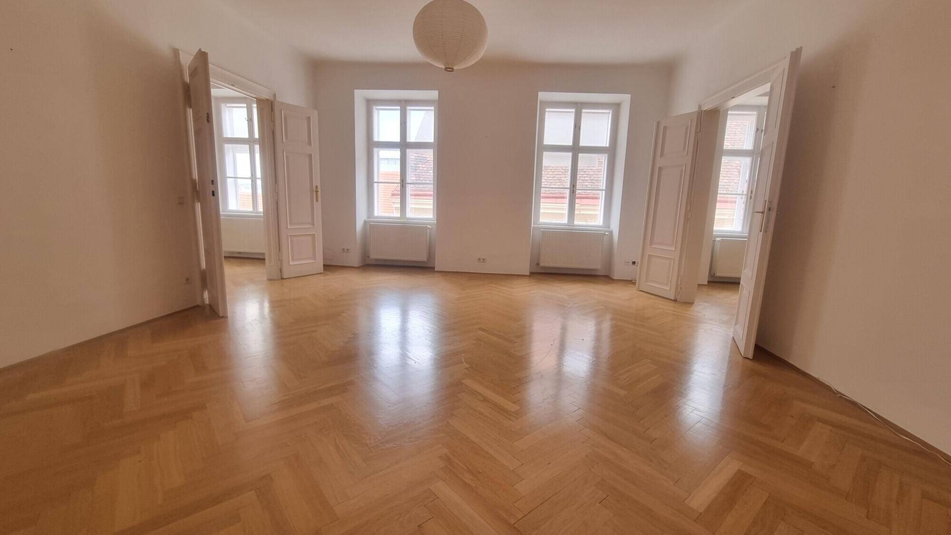 Heller Raum mit elegantem Fischgrätparkett und mehreren Türen, die zu angrenzenden Zimmern führen.