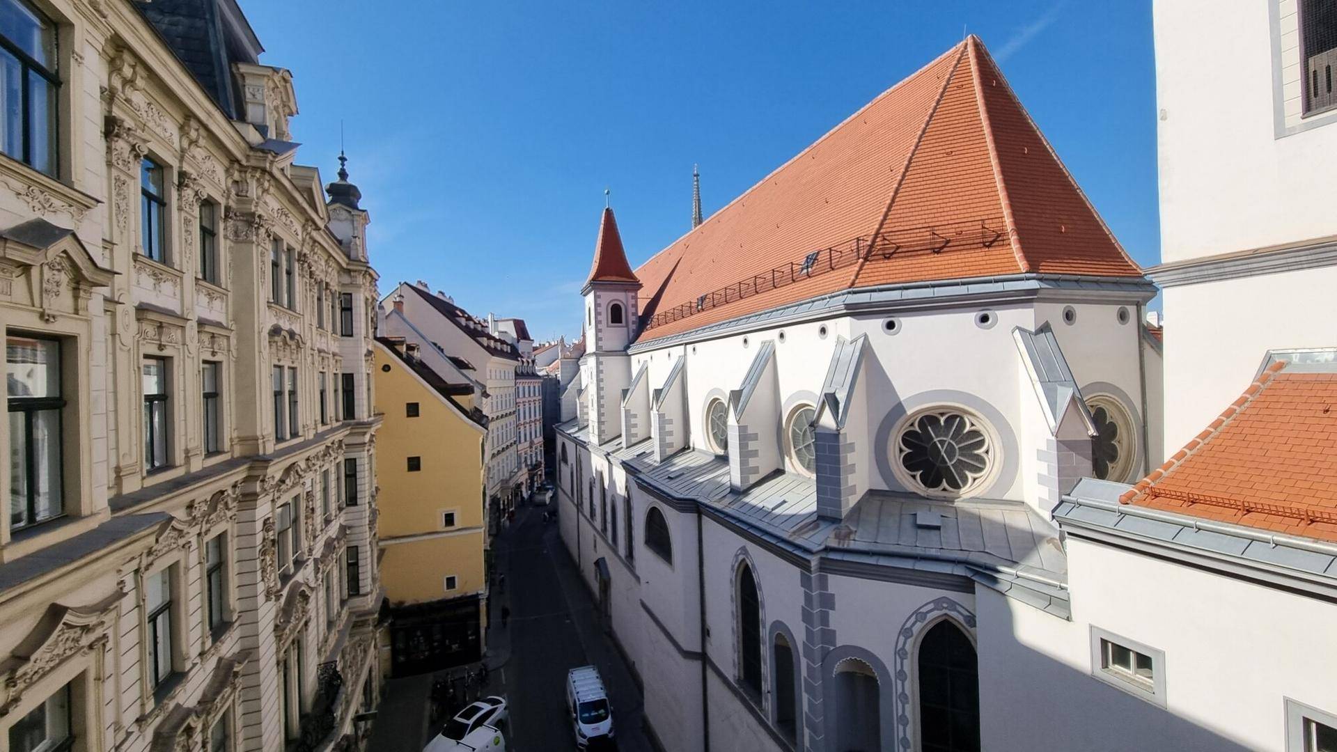 Historische Gebäude und eine Kirche in einer malerischen Altstadtgasse unter blauem Himmel.