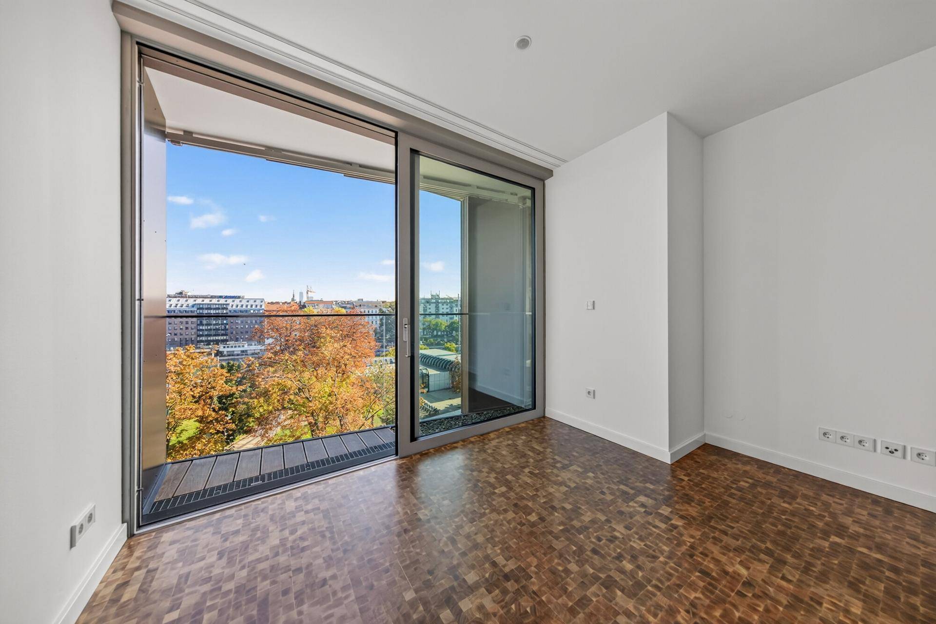Helles Zimmer mit Holzboden und großer Schiebetür zum Balkon mit Stadtblick.