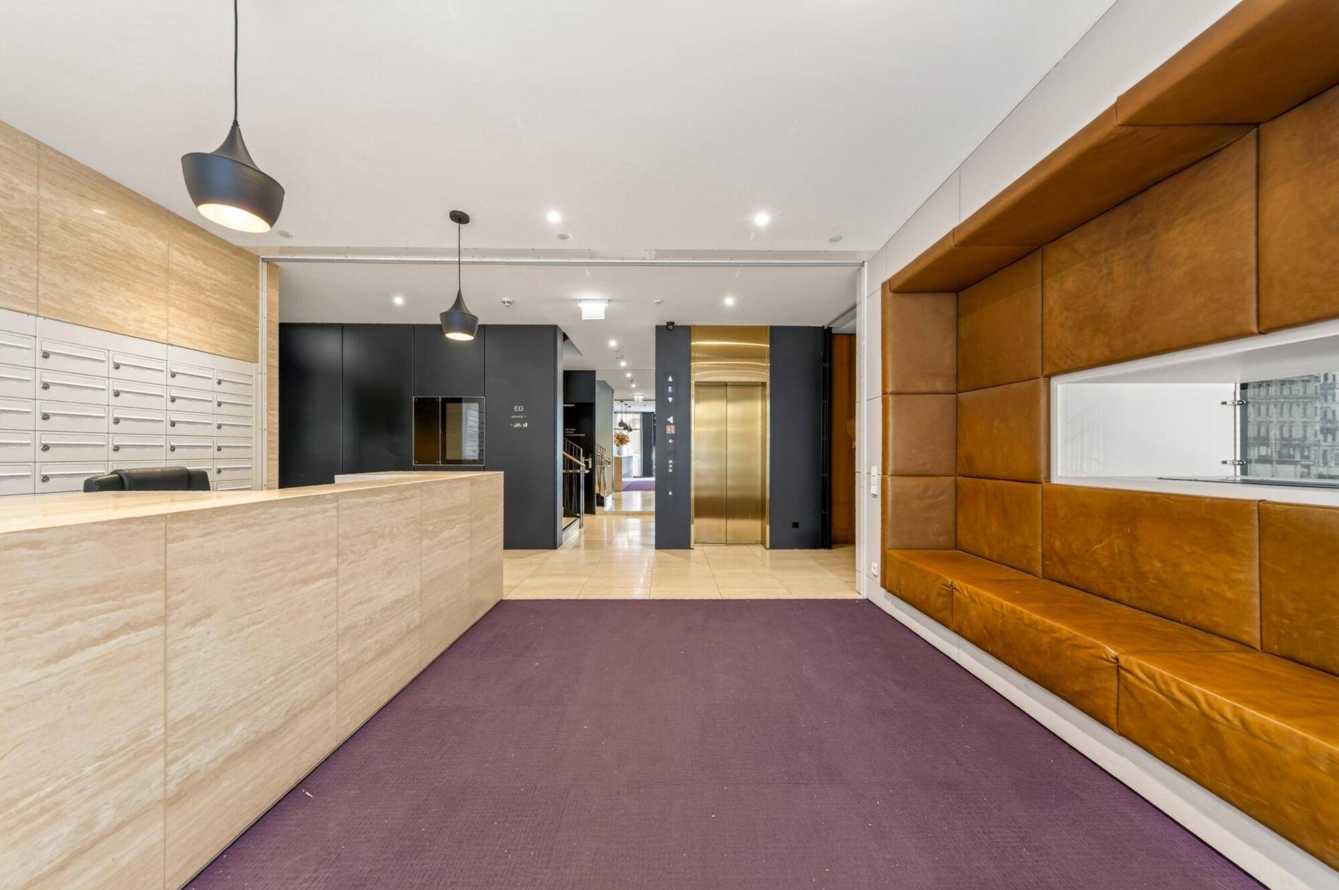 Elegante Lobby mit Rezeption, Sitzgelegenheiten und Aufzugzugang in einem modernen Gebäude.