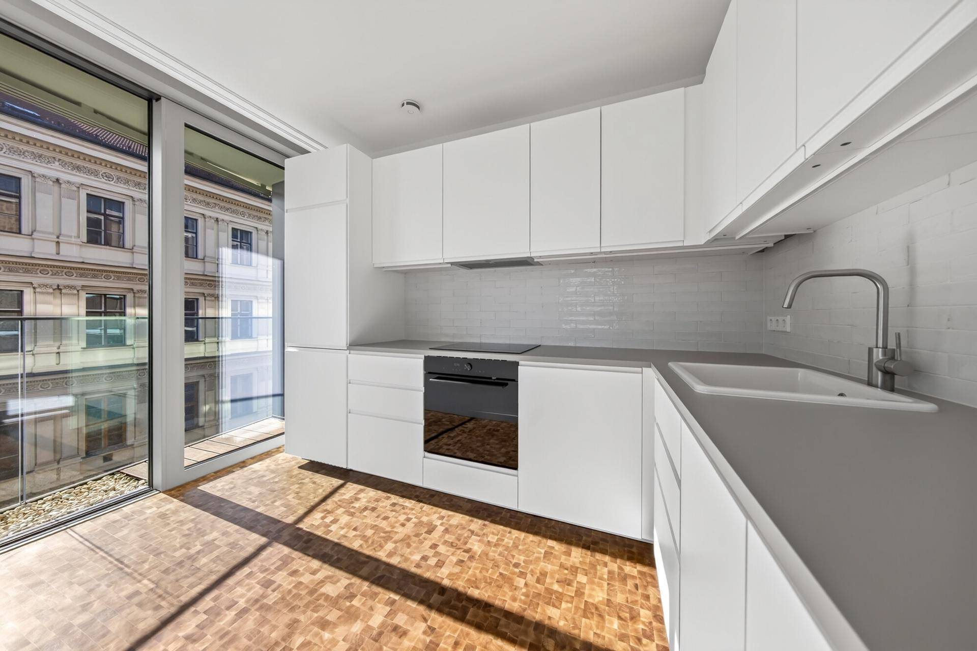 Moderne weiße Küche mit Einbaugeräten, Fliesenrückwand und Zugang zum Balkon.