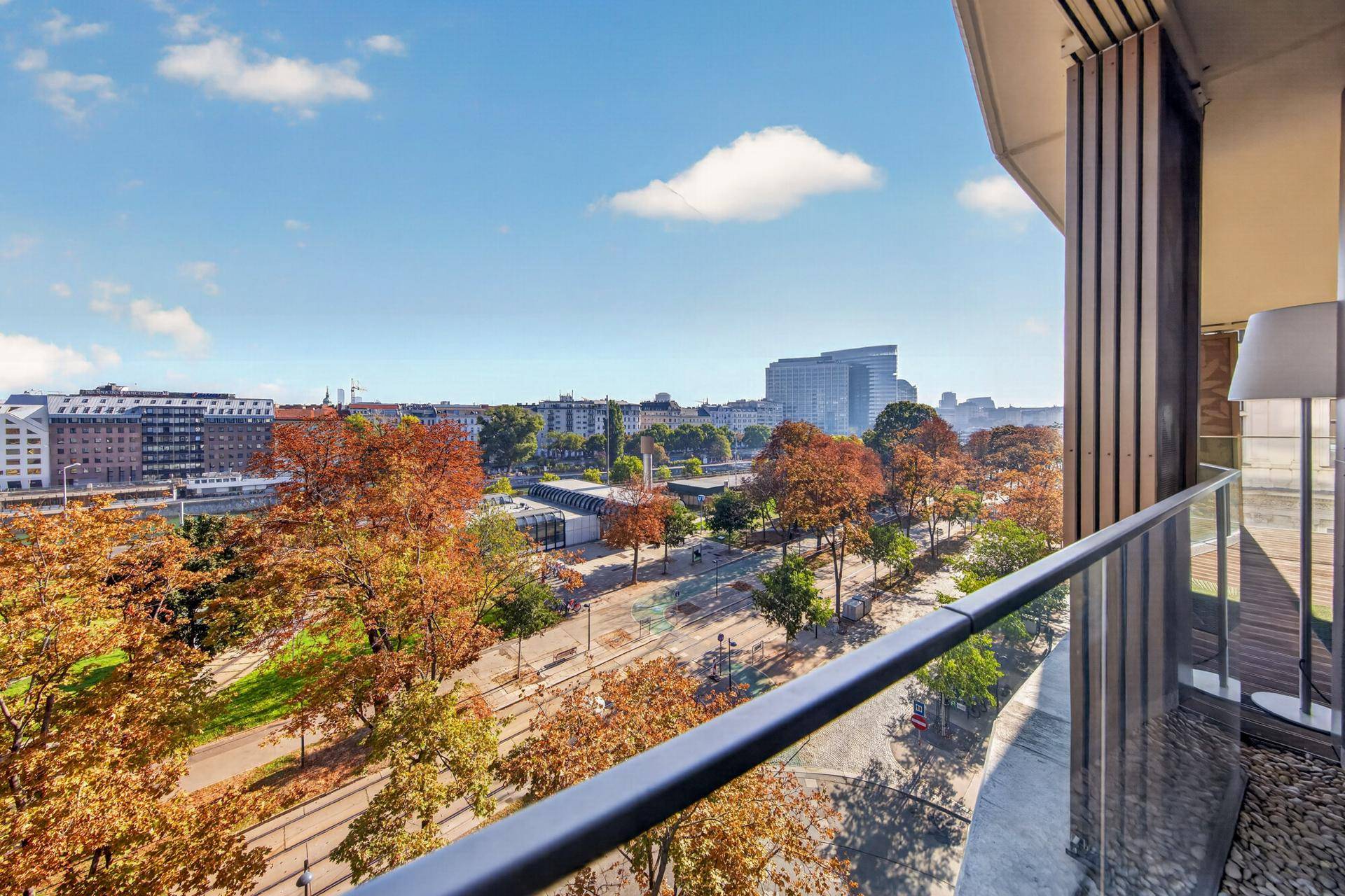 Geräumiger Balkon mit Glasgeländer und Panoramablick auf die herbstliche Stadtlandschaft.