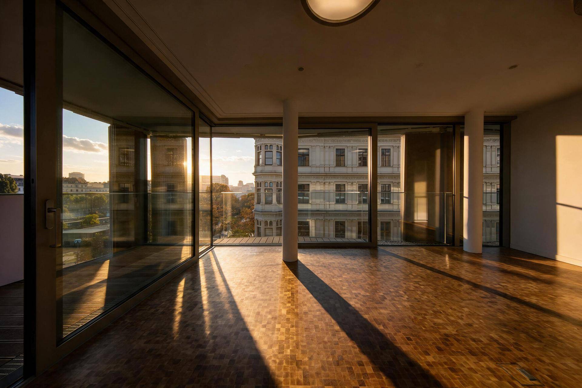 Wohnzimmer mit Holzboden und großen Fenstern, durch die die Abendsonne scheint.