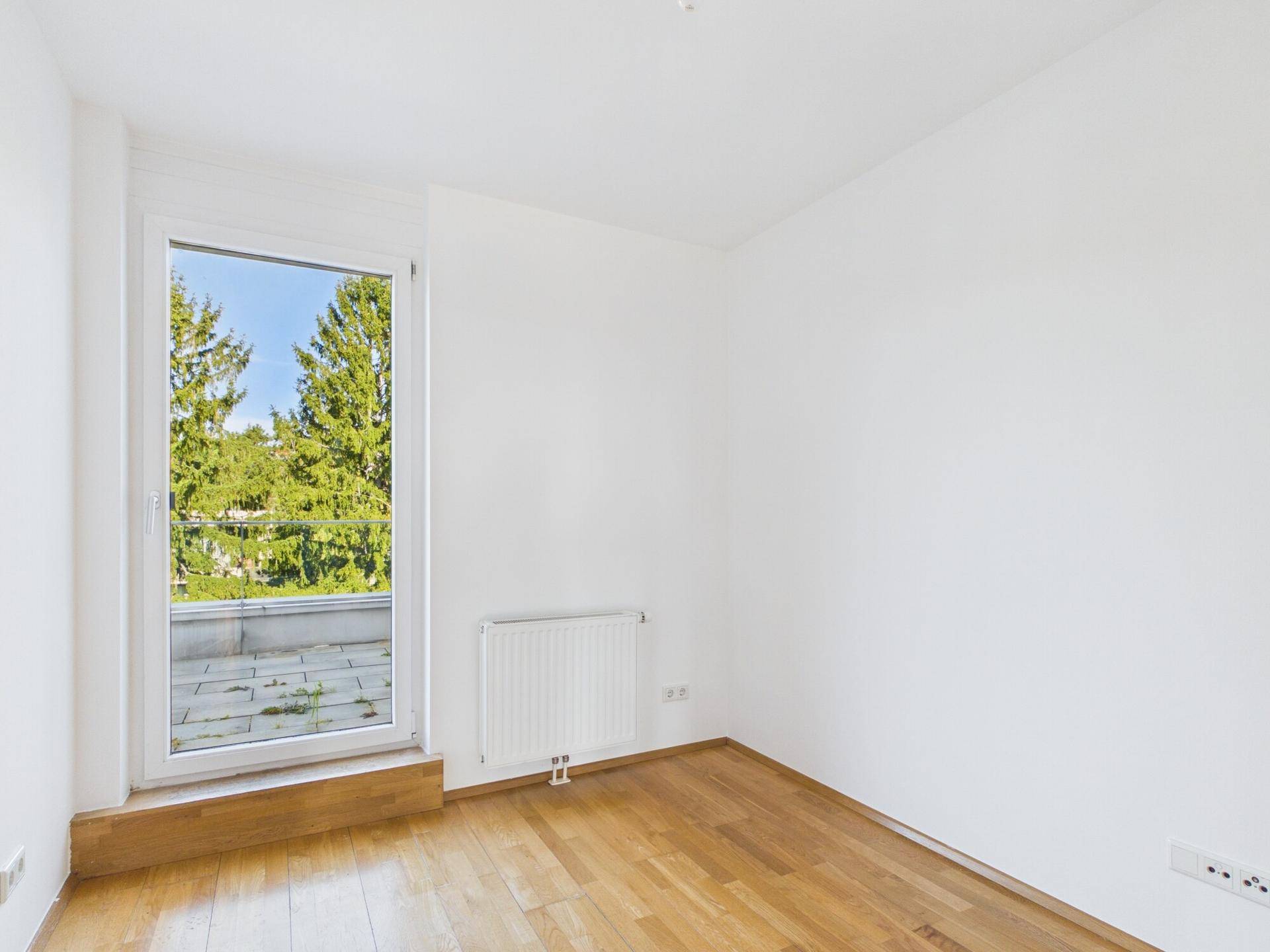 Leeres Schlafzimmer mit Holzboden, großem Fenster und Zugang zu einer Terrasse.