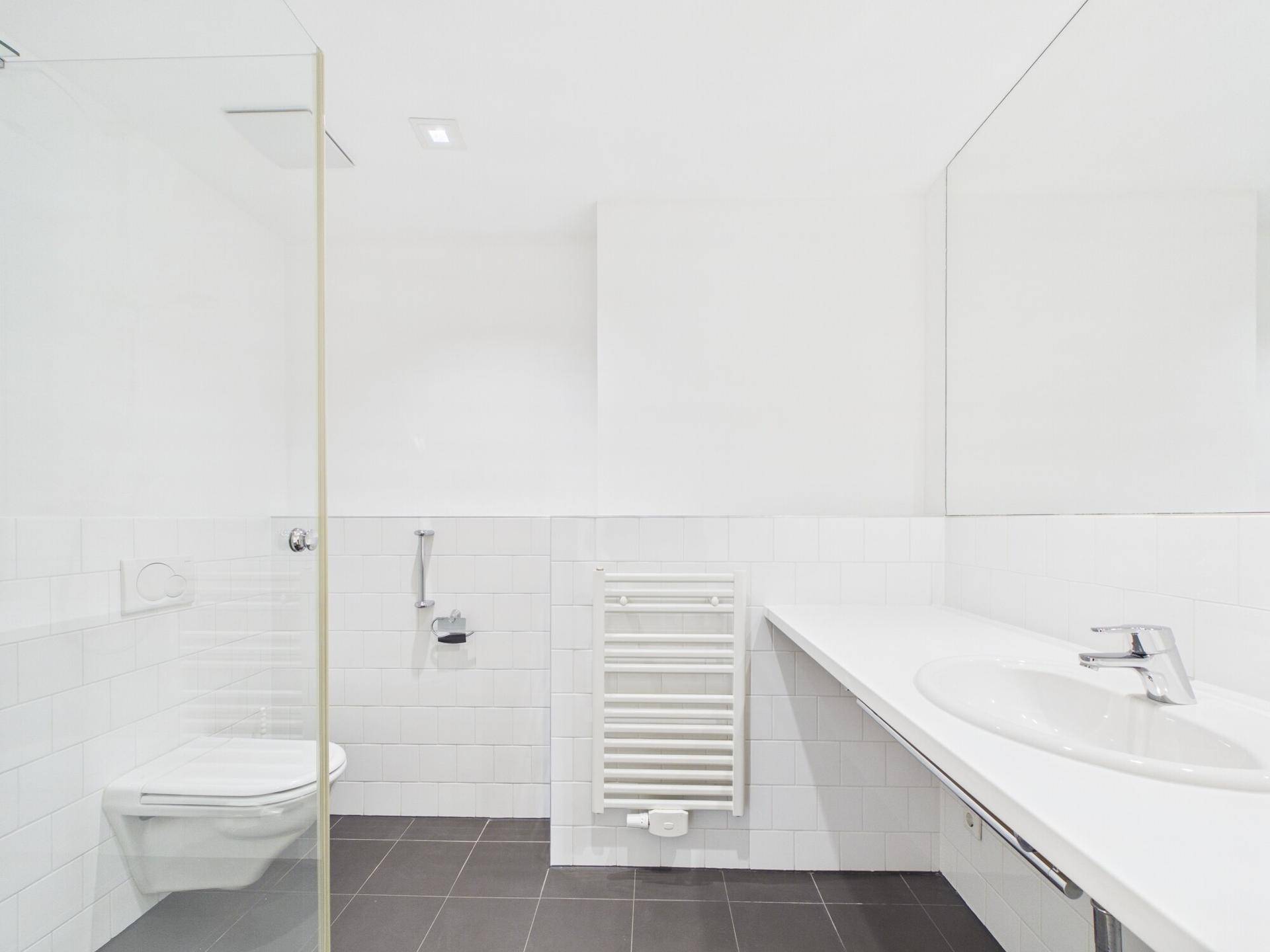 Modernes Badezimmer mit ebenerdiger Dusche, Wand-WC und beheiztem Handtuchhalter.
