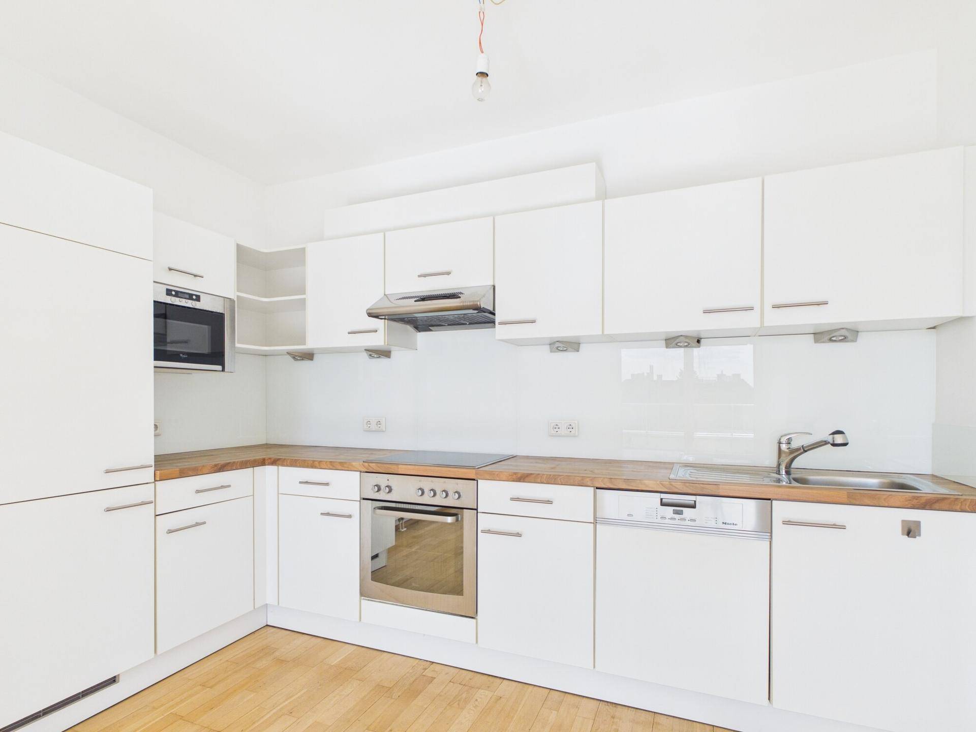 Moderne Einbauküche in Weiß mit Holz-Arbeitsplatten und integrierten Geräten.