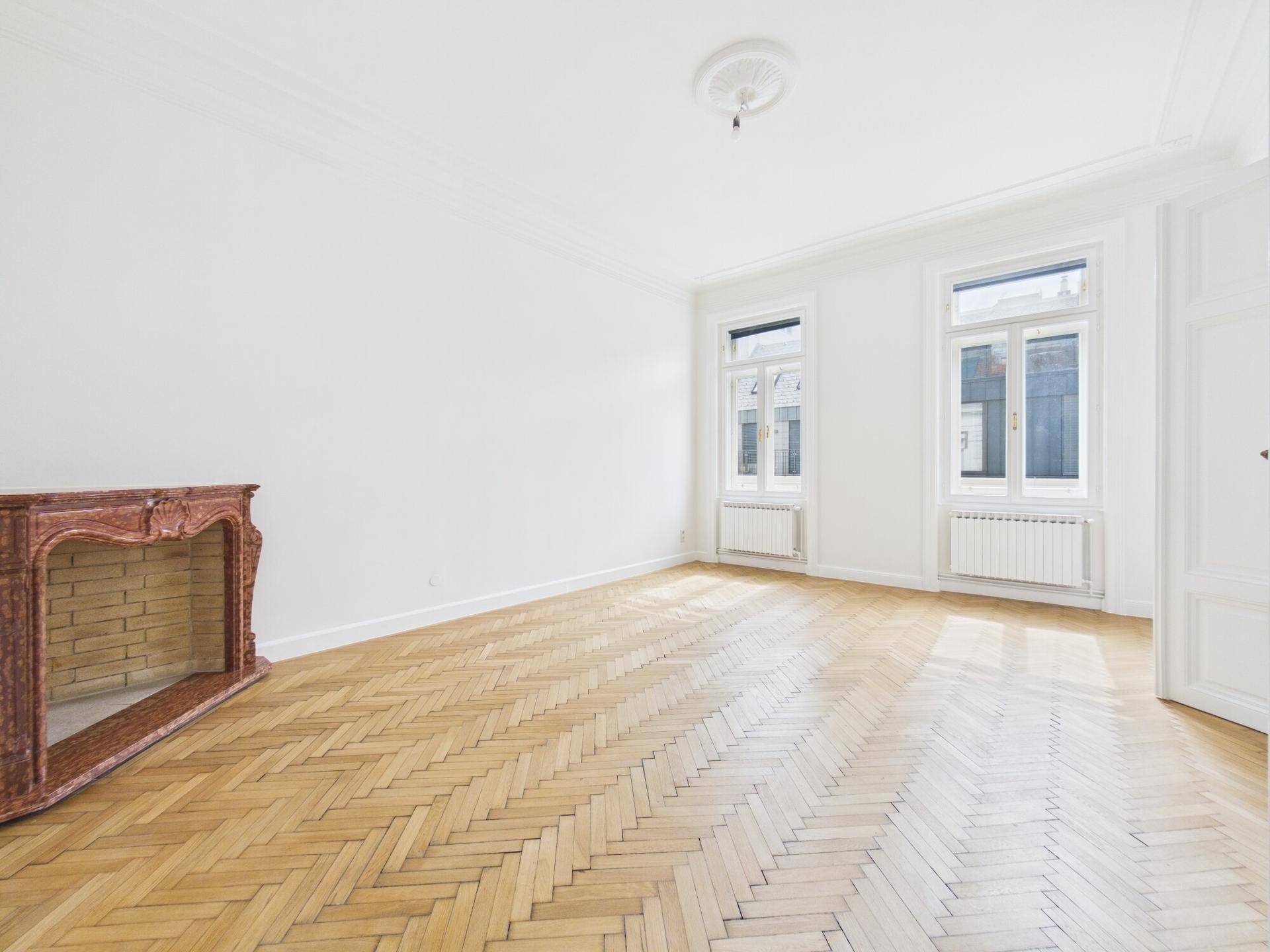 Elegantes Zimmer mit Fischgrätparkett, hohen Decken und einem dekorativen Kamin.