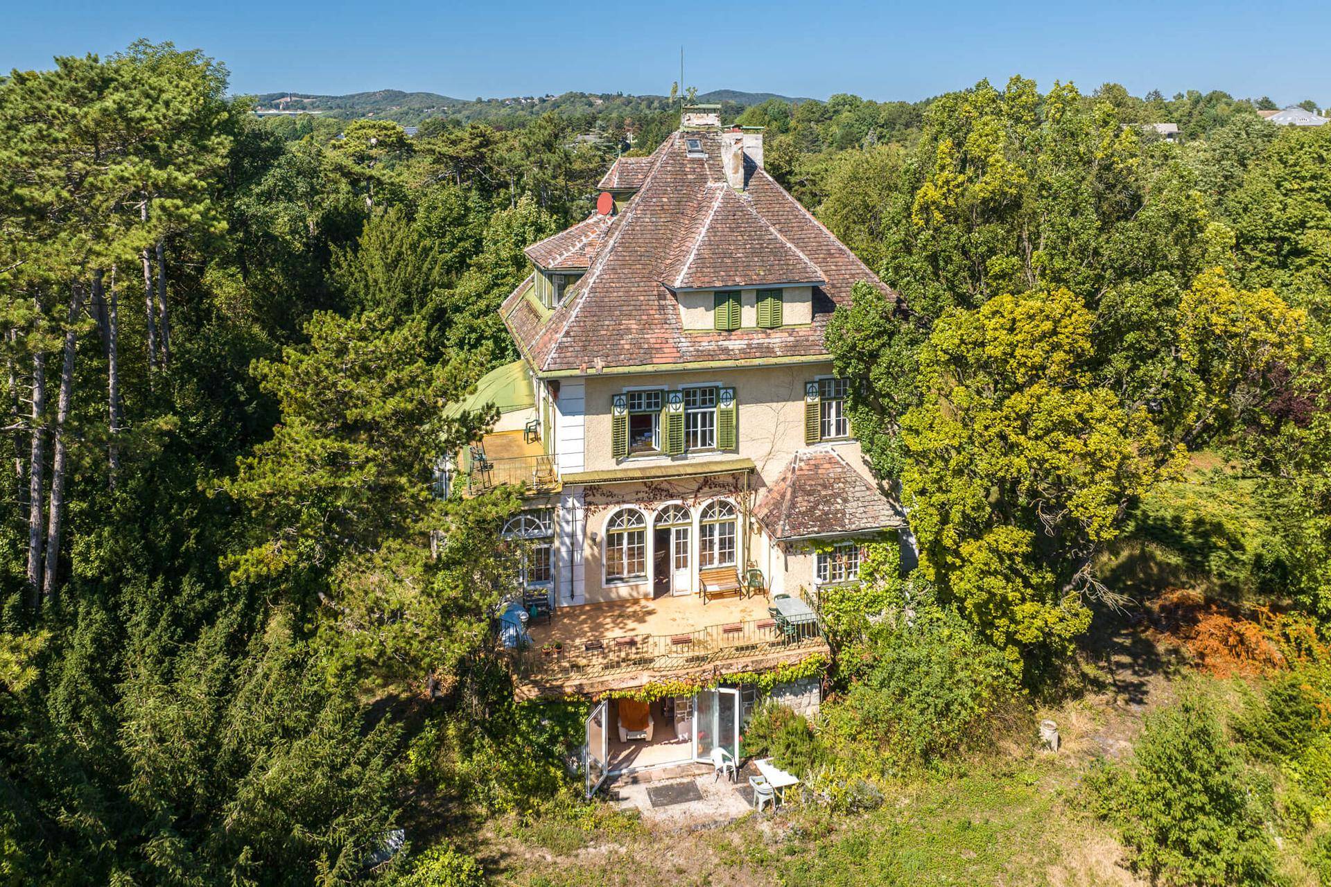 Luftaufnahme der historischen Villa, eingebettet in eine grüne Hügellandschaft mit dichtem Baumbestand.