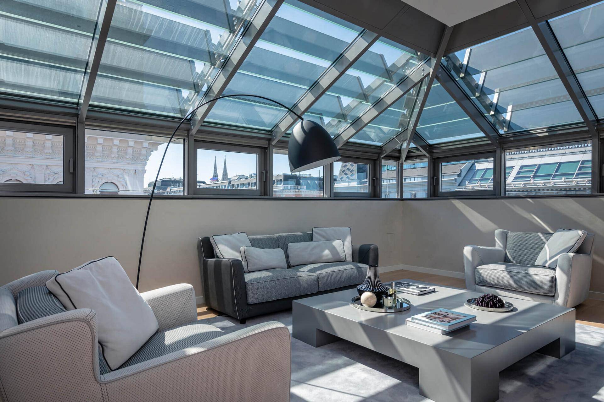 Gemütlicher Wohnbereich unter einem Glasdach mit bequemen Sofas und Blick auf die Stadt.