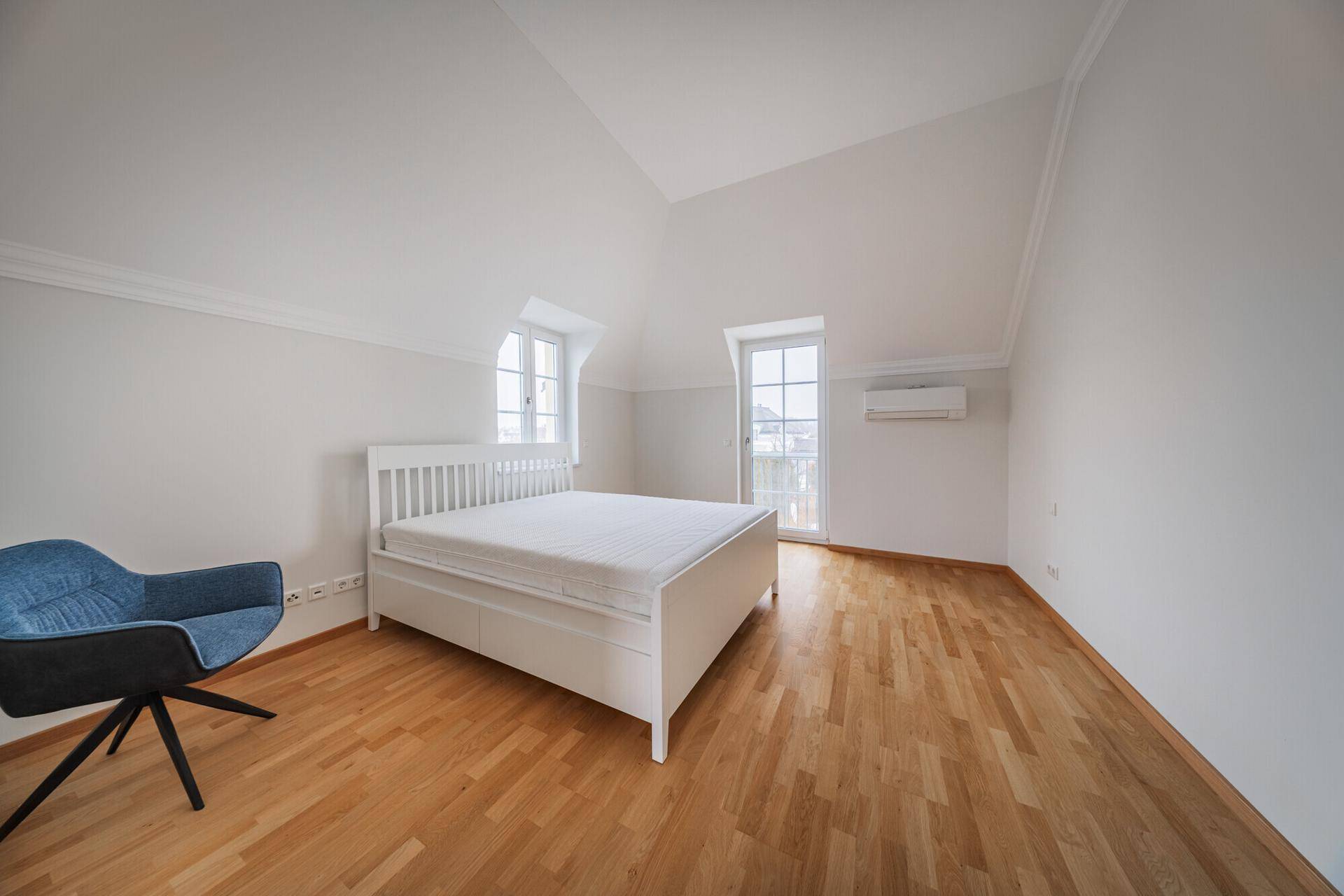 Helles Schlafzimmer mit Holzboden, Dachschrägen und Zugang zu einem französischen Balkon.