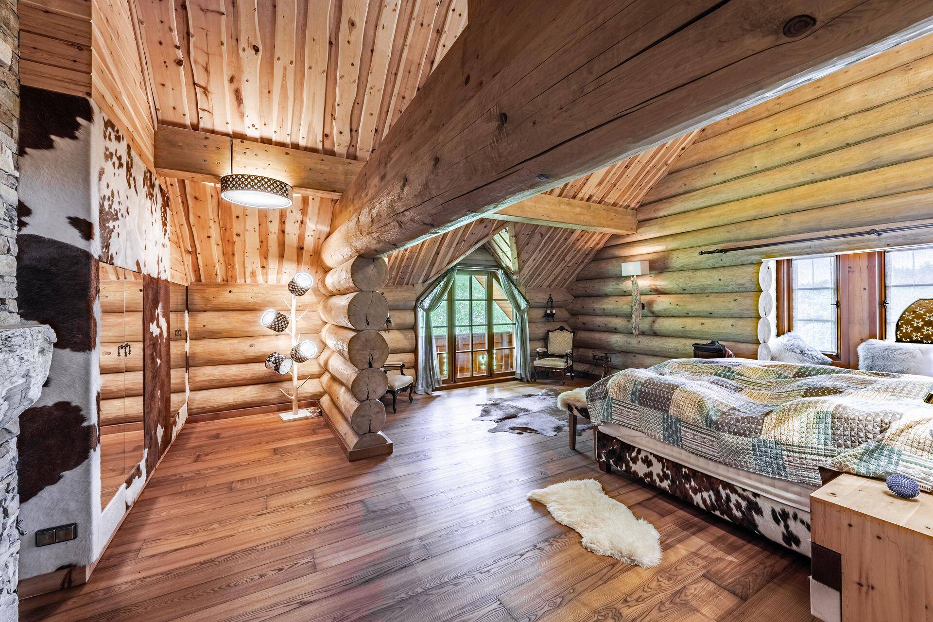 Geräumiges Schlafzimmer im Chalet-Stil mit Holzbalken, großen Fenstern und Kuhfell-Akzenten.