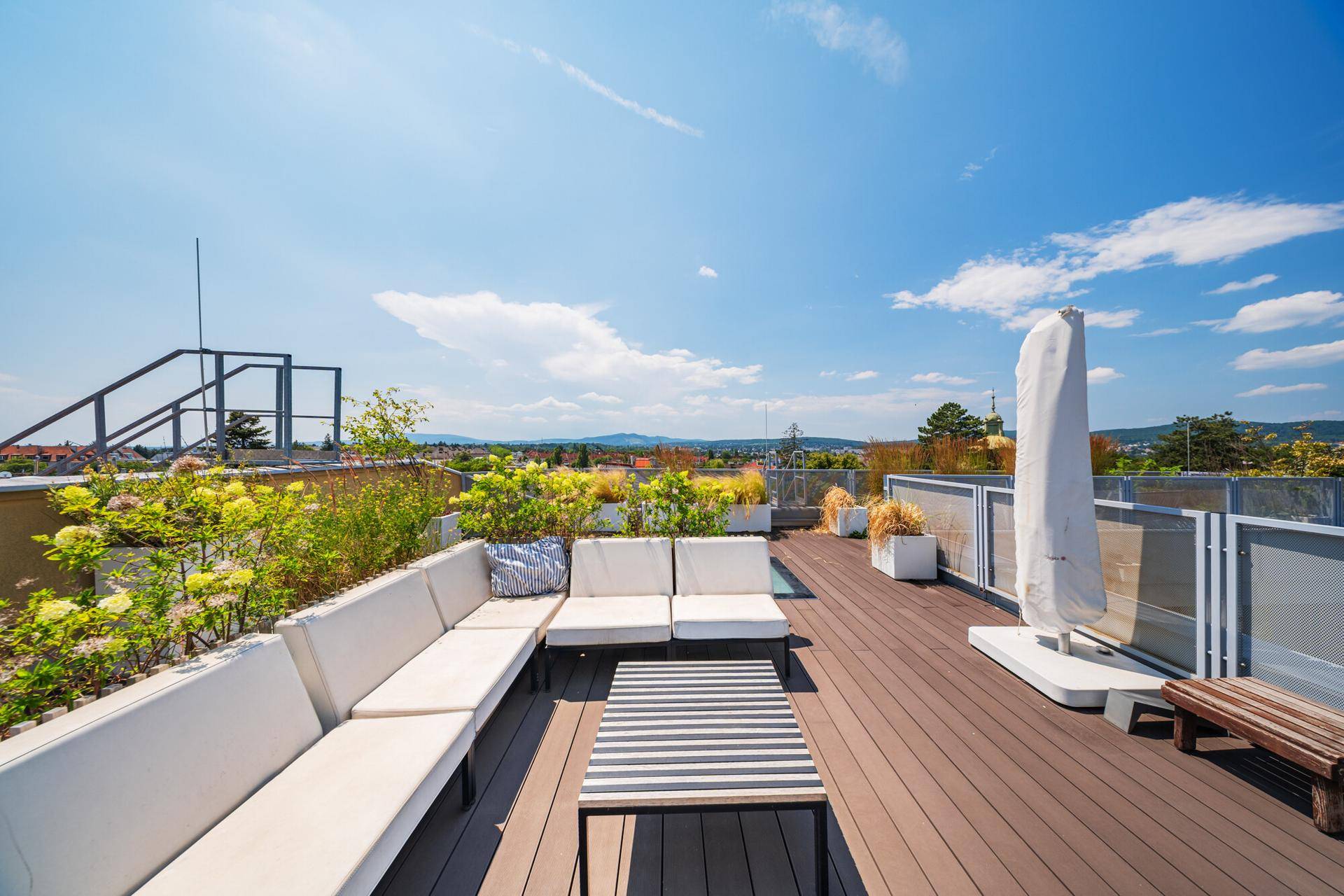 Gemütliche Dachterrasse mit Lounge-Möbeln, Pflanzen und einem weiten Blick über die Landschaft.