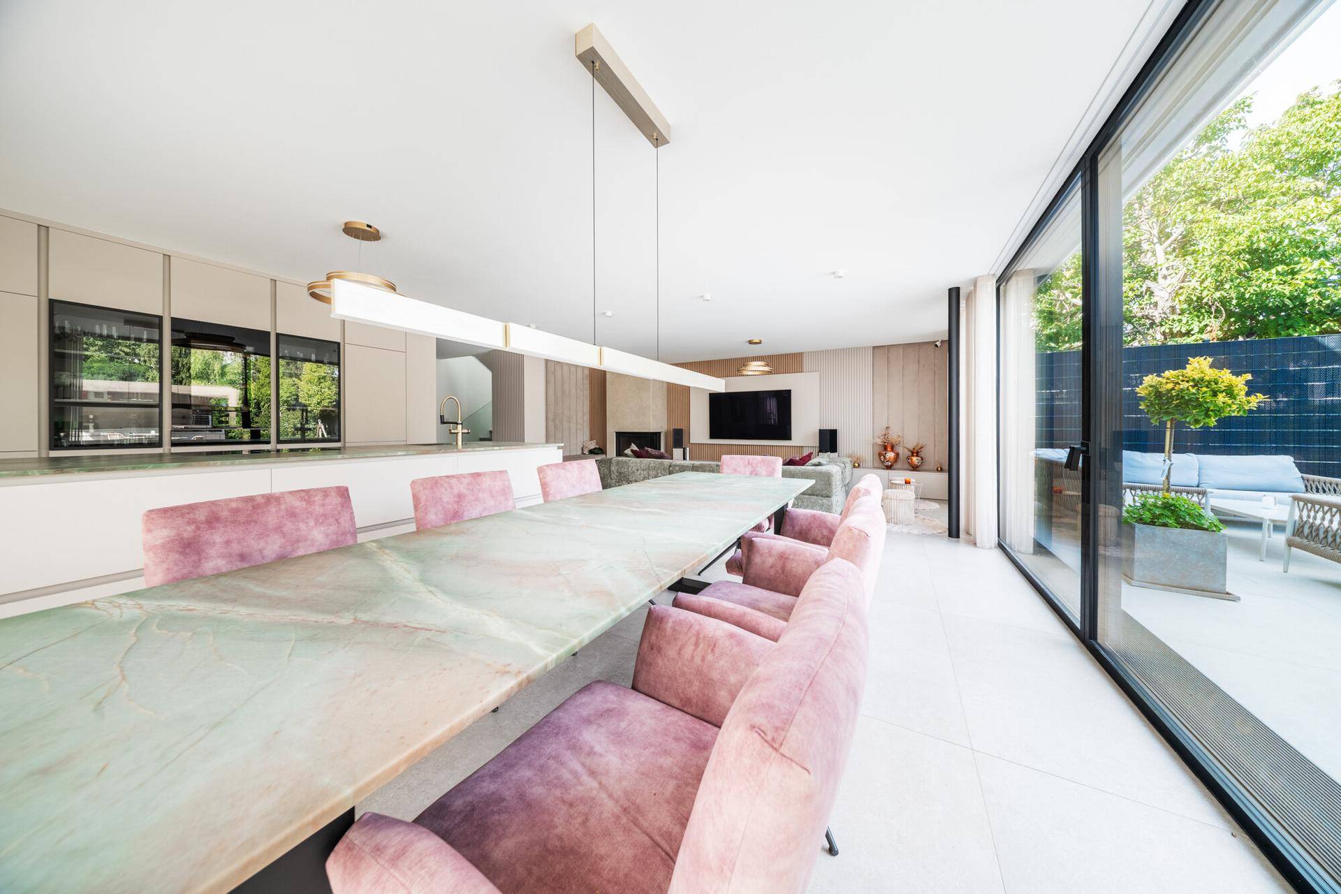 Eleganter Essbereich mit langem Tisch, rosa Stühlen und raumhohen Fenstern mit Zugang zur Terrasse.