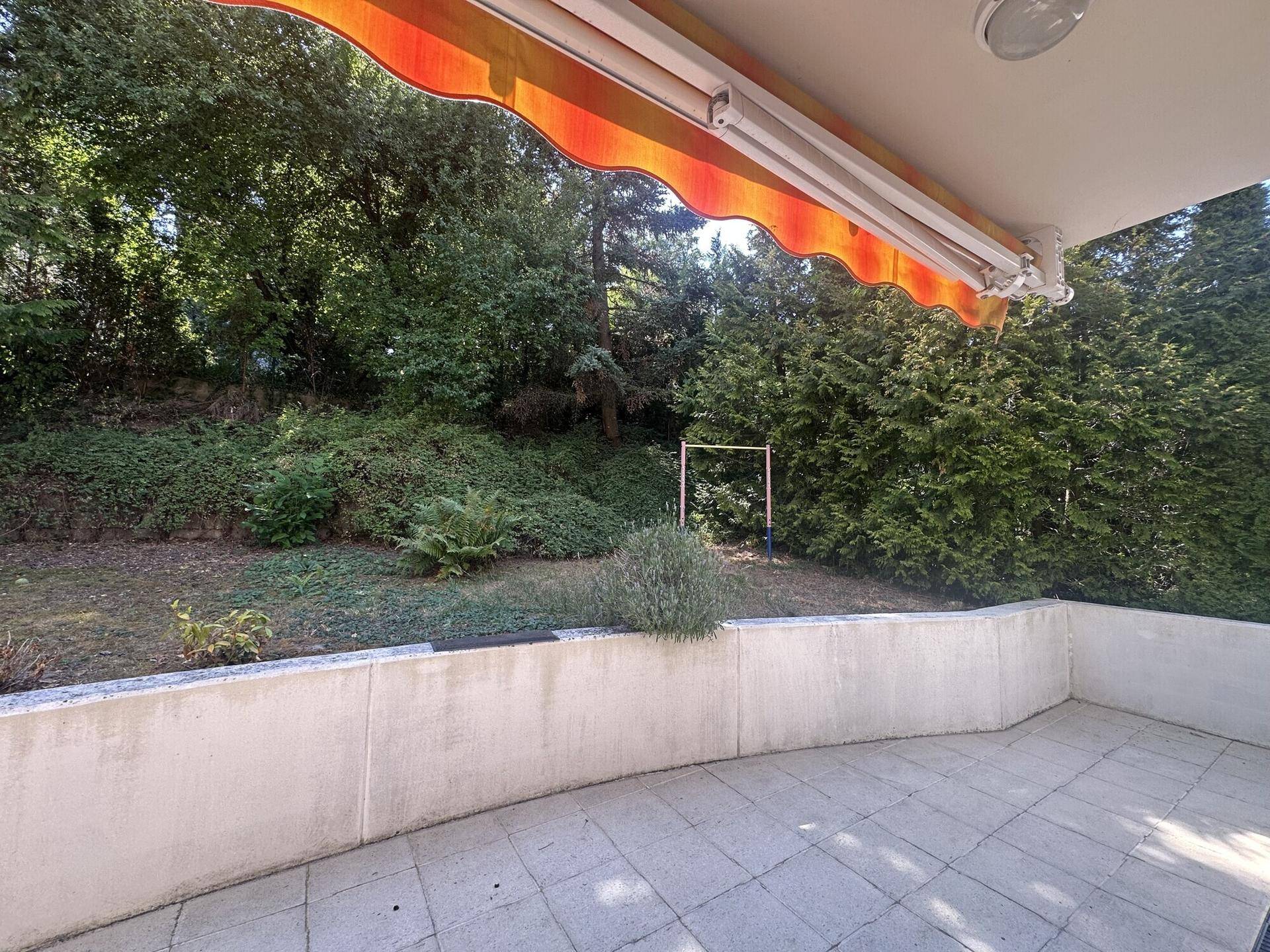 Geräumige Terrasse mit Markise und Blick auf den privaten Gartenbereich mit viel Grün.