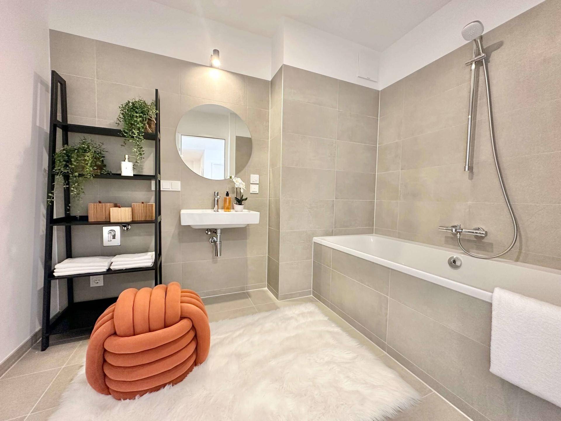 Modernes Badezimmer mit Badewanne, Waschtisch und hellen Fliesen, ergänzt durch einen dekorativen Teppich.