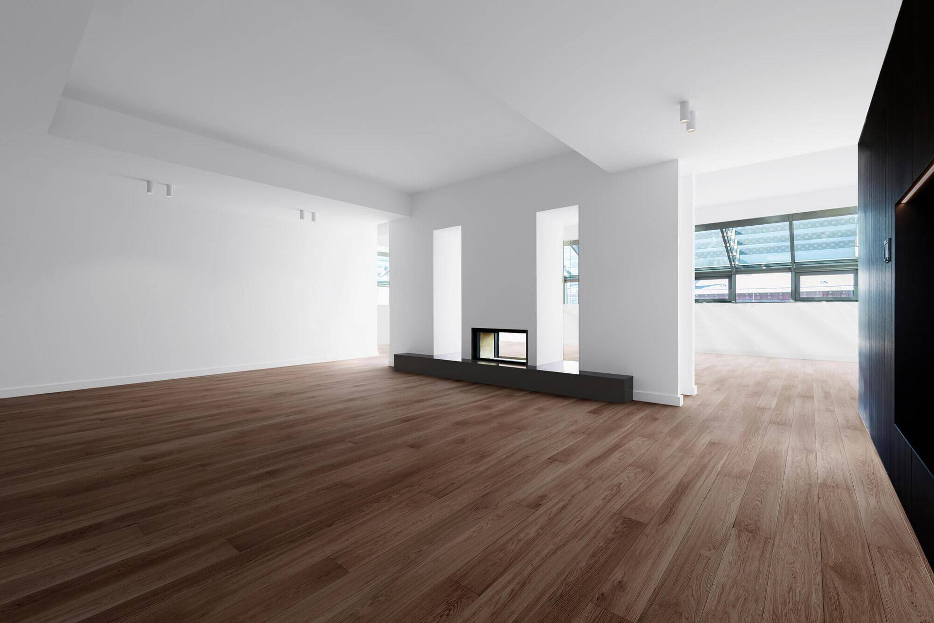 Geräumiger, unmöblierter Wohnbereich mit dunklem Holzboden und integriertem Kamin, bereit zur Gestaltung.