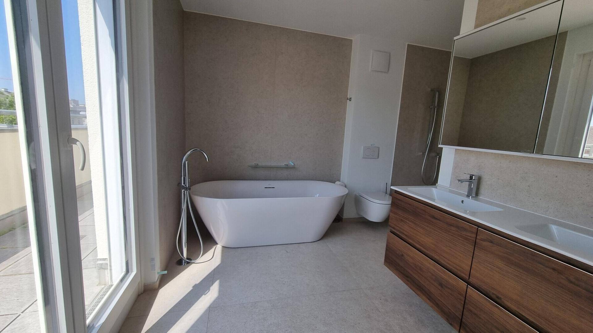 Modernes Badezimmer mit freistehender Badewanne, Holzwaschtisch und Zugang zur Terrasse.