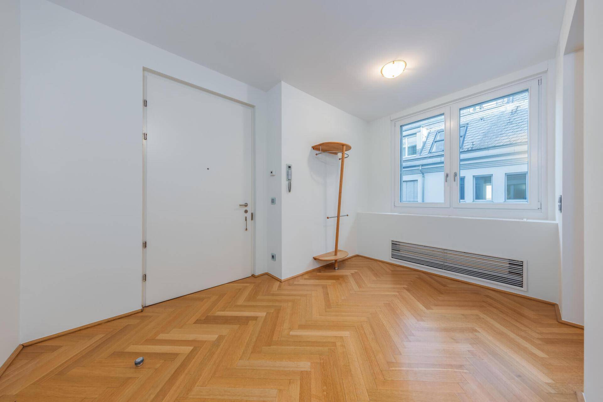 Heller Eingangsbereich mit Fischgrätparkett, weißer Tür und Fenster mit Blick auf die Umgebung.