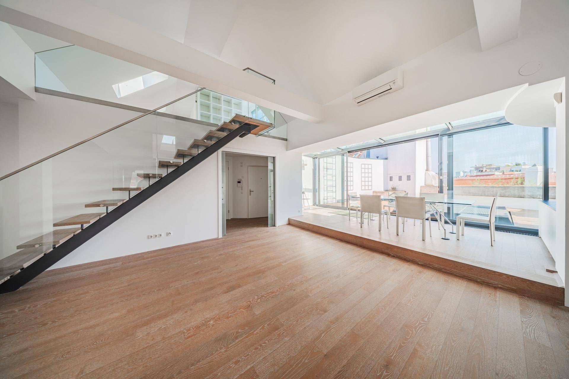 Heller, offener Wohn-Essbereich mit Holzparkett, moderner Treppe und großen Glasfronten.