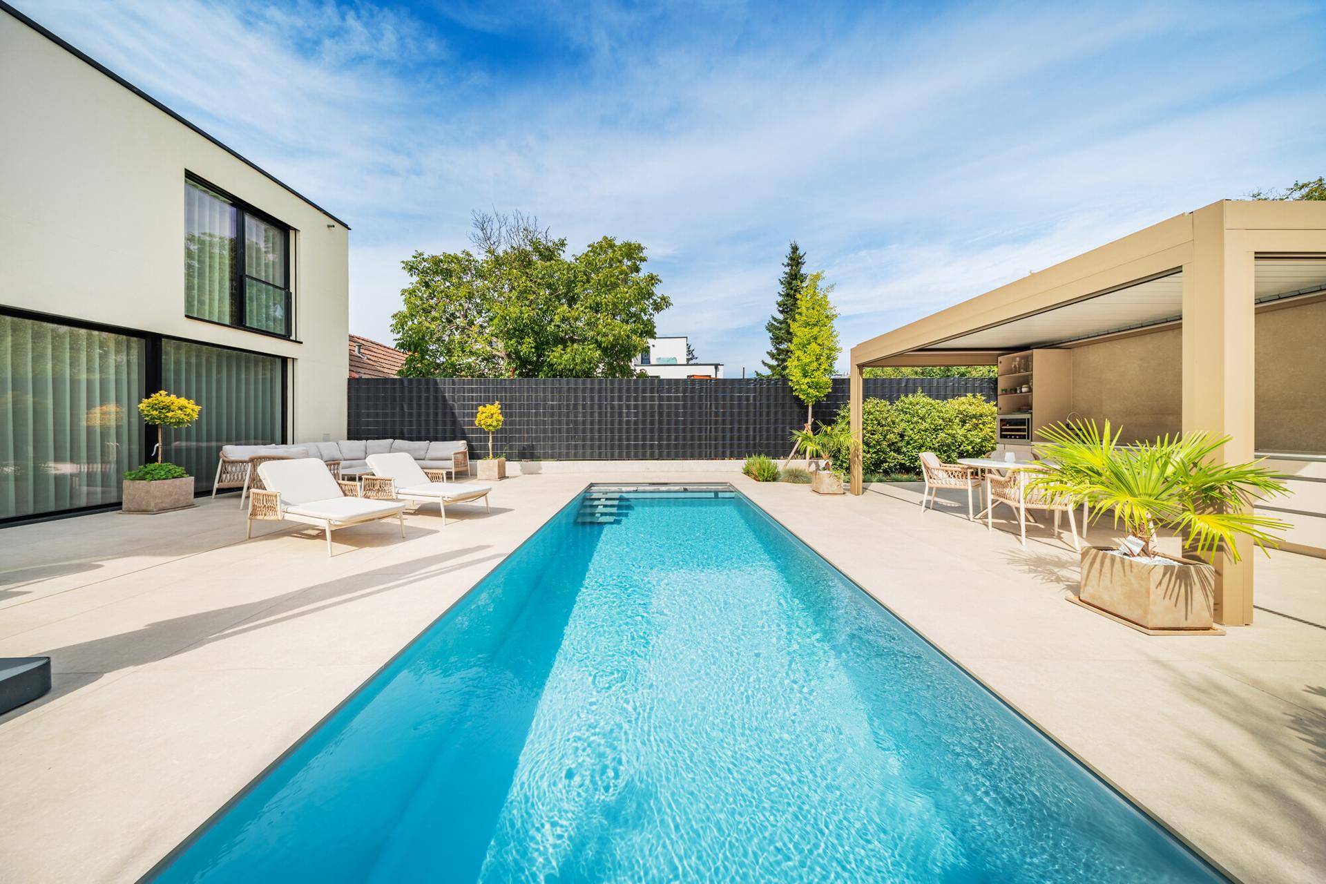 Elegante Poolanlage mit weitläufiger Sonnenterrasse, modernen Liegestühlen und einer überdachten Außenküche.