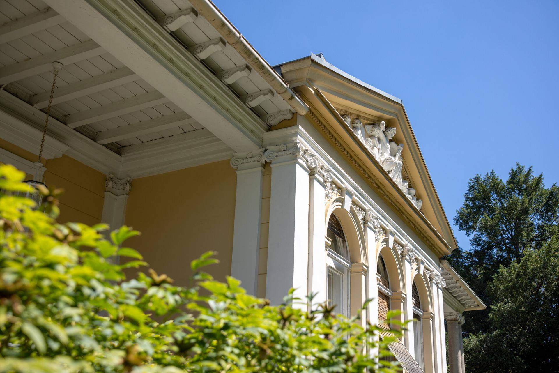 Detailansicht der eleganten Fassade mit Säulen, Stuckverzierungen und Giebelschmuck.