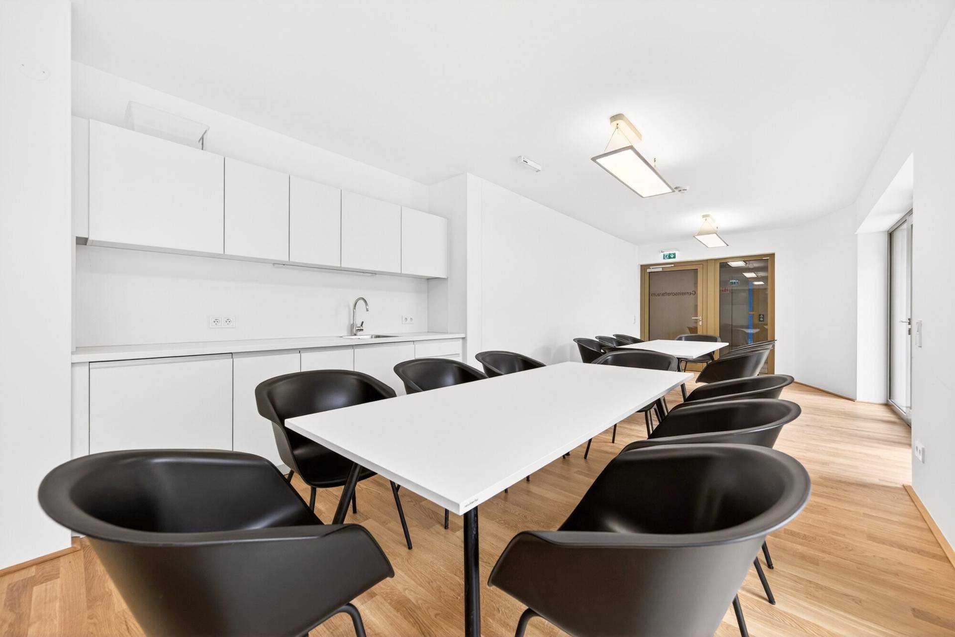 Gemeinschaftsraum mit Tischen, Stühlen und einer integrierten Küchenzeile.