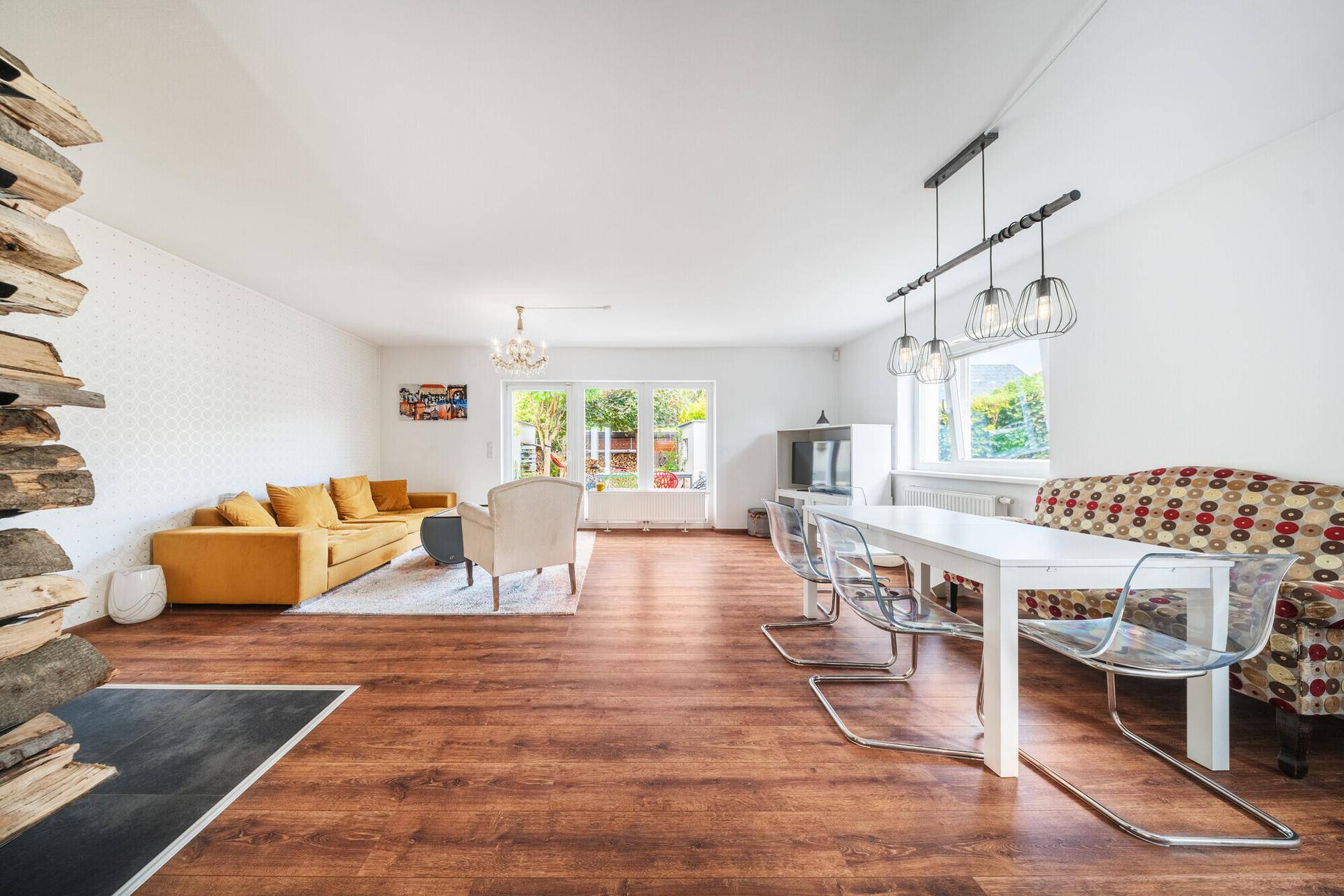 Geräumiger Wohn-Essbereich mit Holzboden, gelbem Sofa und transparenten Esszimmerstühlen.