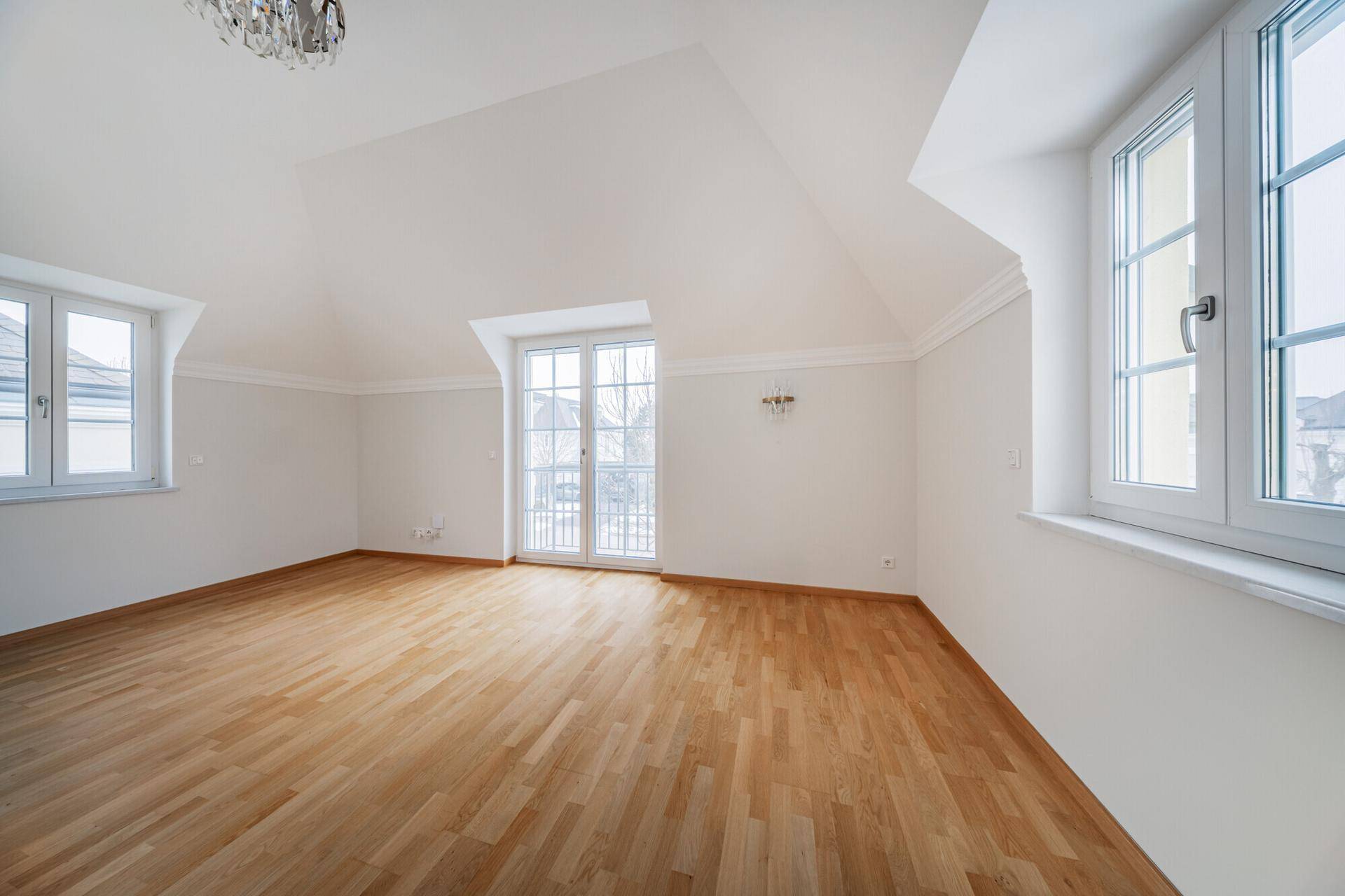 Helles Zimmer im Dachgeschoss mit Holzboden, Dachschrägen und Zugang zu einem Balkon.