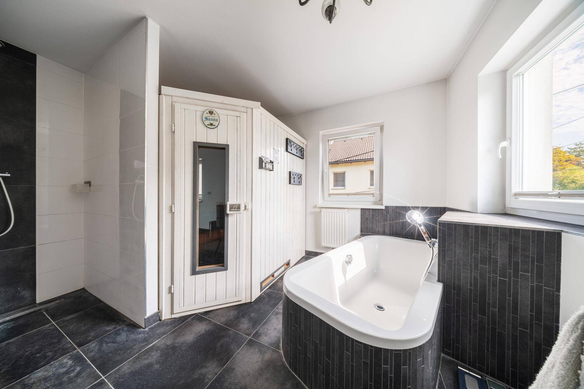 Modernes Badezimmer mit Badewanne, Dusche, integrierter Sauna und Fenster.