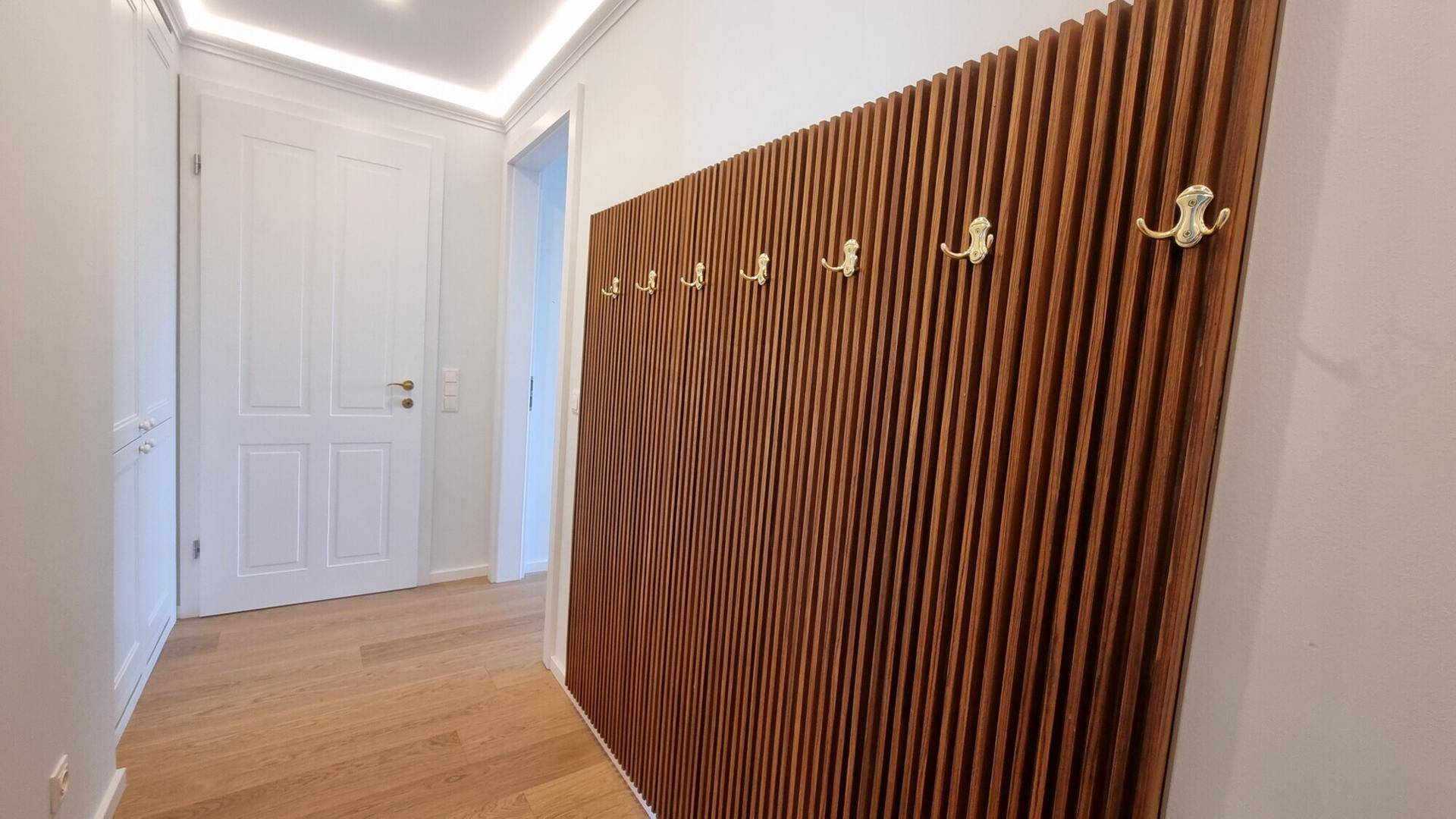 Heller Flur mit einer dekorativen Holzlamellenwand und praktischen Garderobenhaken.