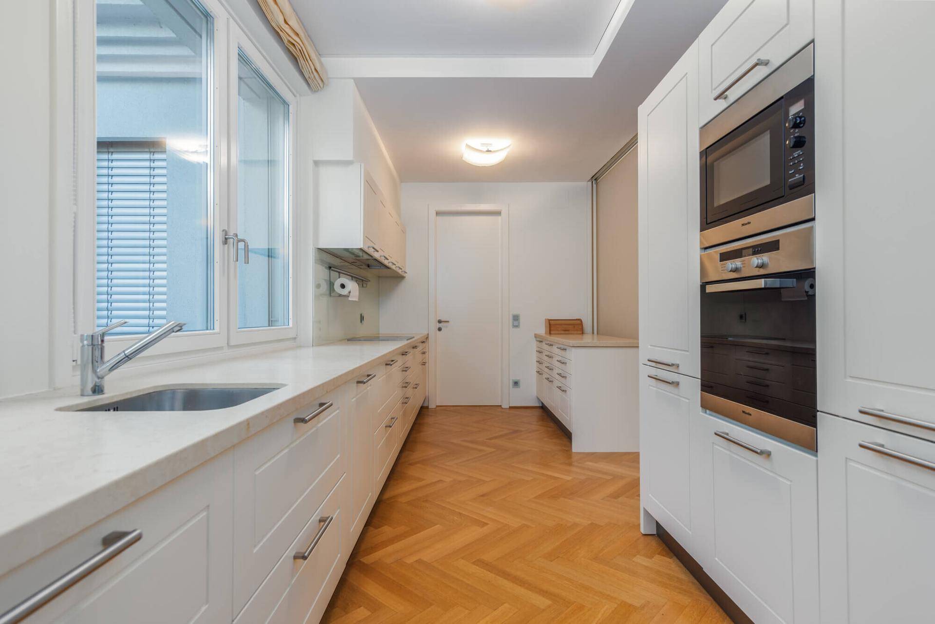 Moderne weiße Einbauküche mit integrierten Geräten und Fenster für natürliches Licht.