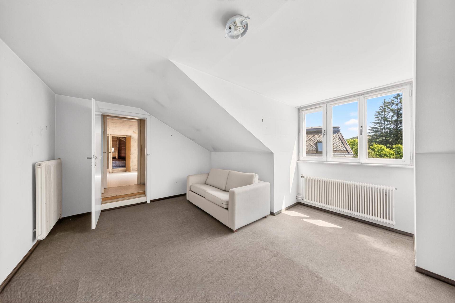 Helles Zimmer im Dachgeschoss mit Schrägen, Teppichboden und Ausblick ins Grüne.