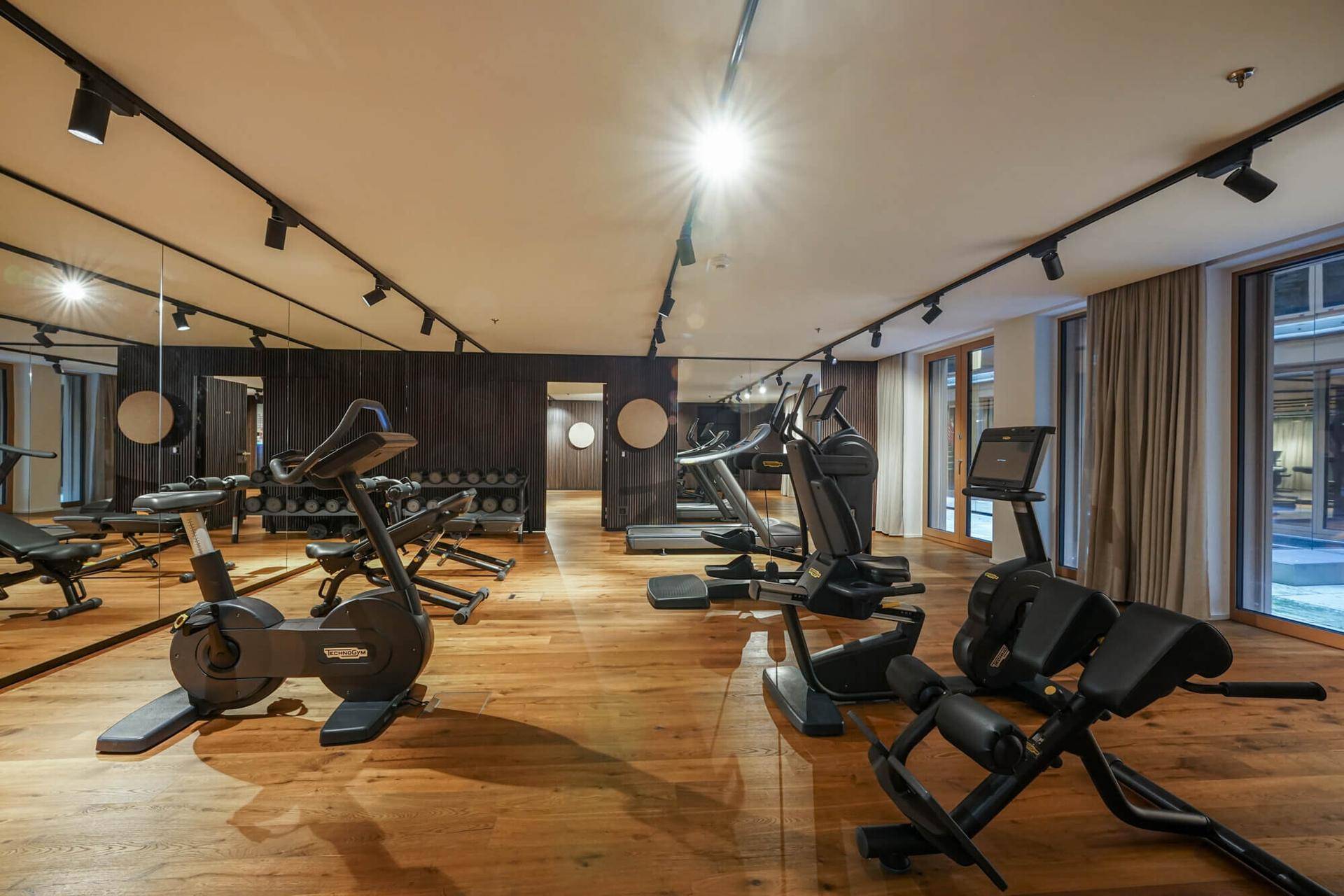 Gut ausgestatteter Fitnessraum mit modernen Trainingsgeräten und Holzfußboden.