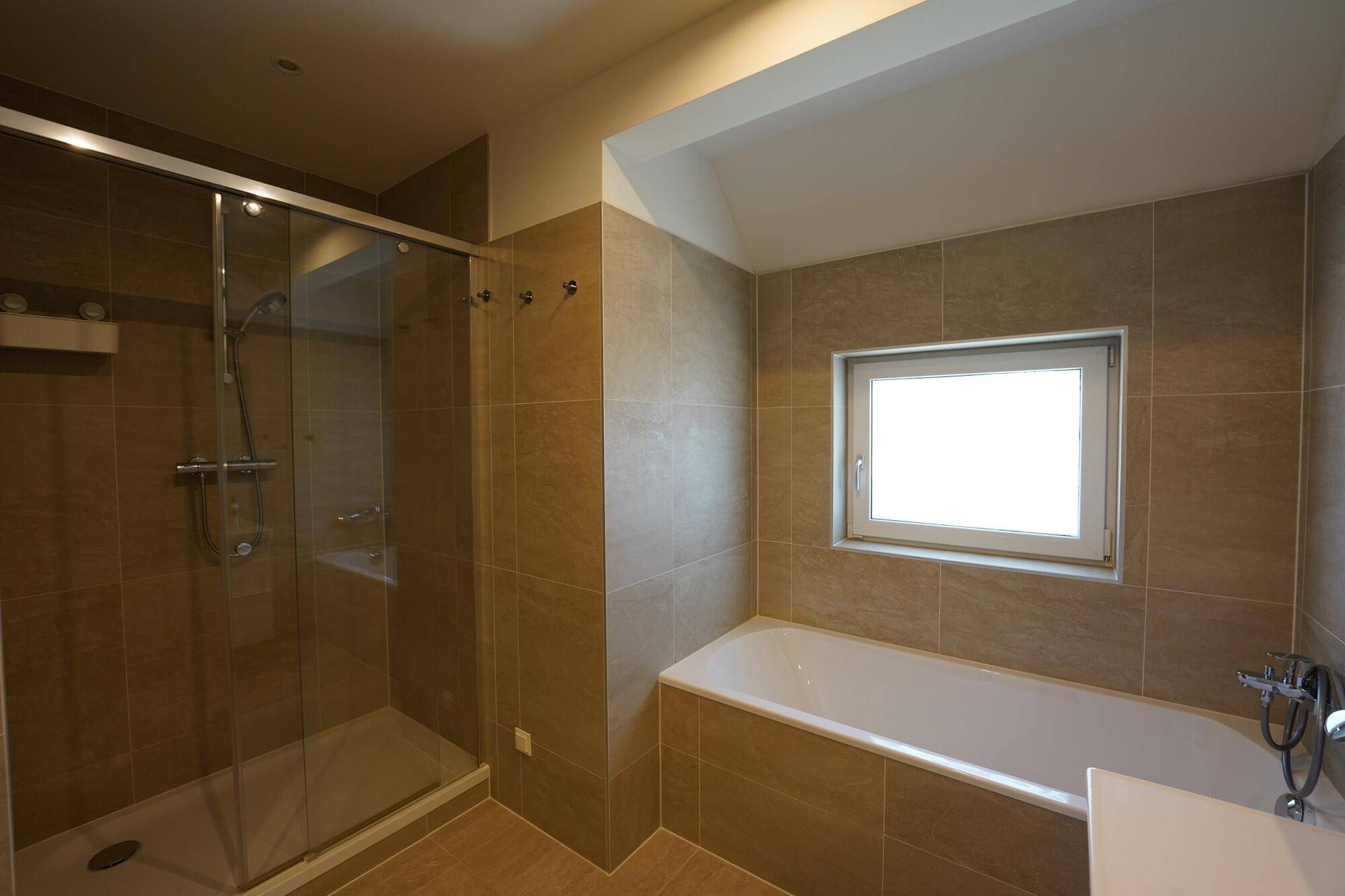 Modernes Badezimmer mit beigefarbenen Fliesen, Badewanne und begehbarer Dusche, inklusive Fenster.