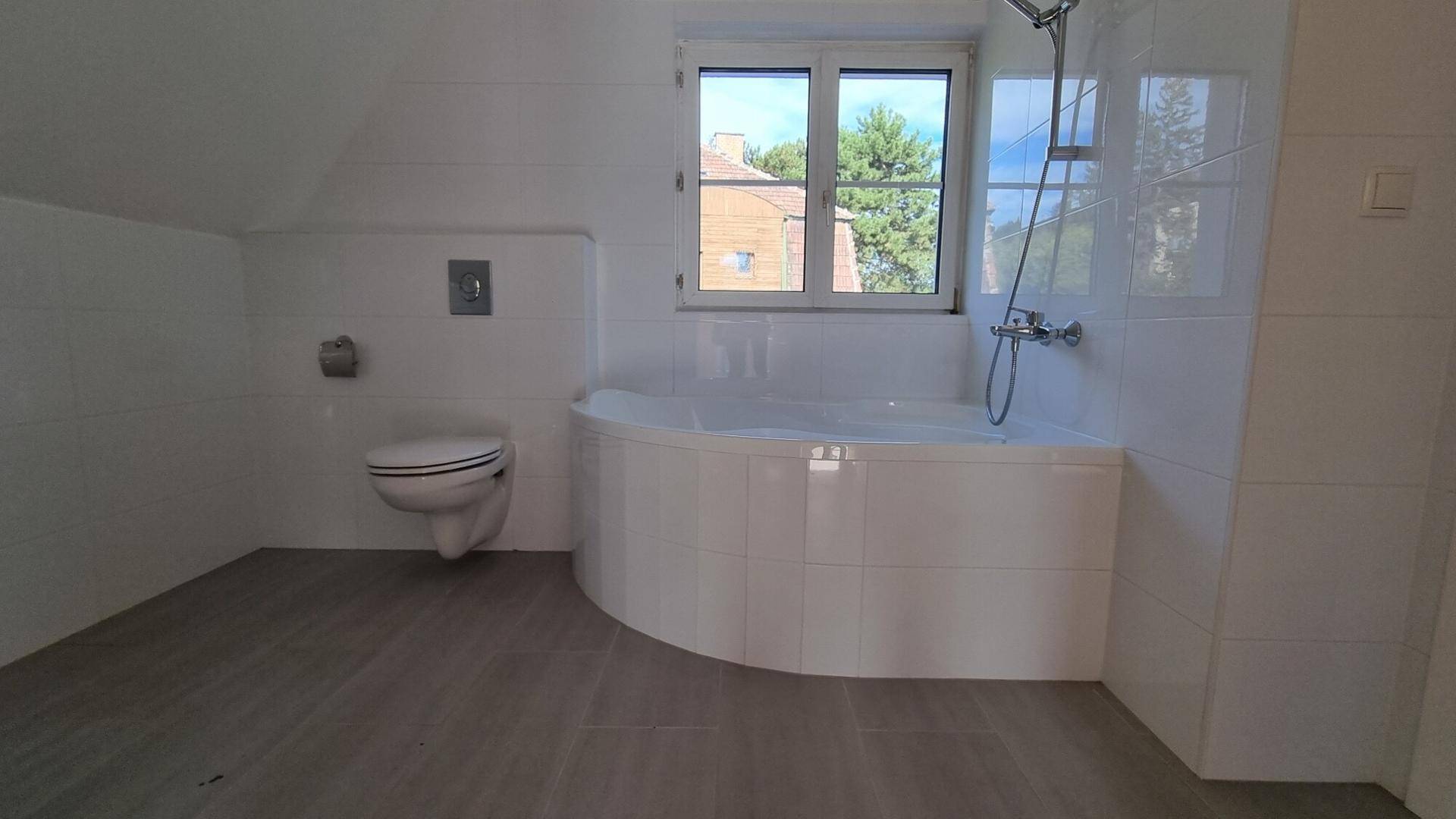 Badezimmer mit Eckbadewanne, wandhängendem WC und Fenster im Dachgeschoss.