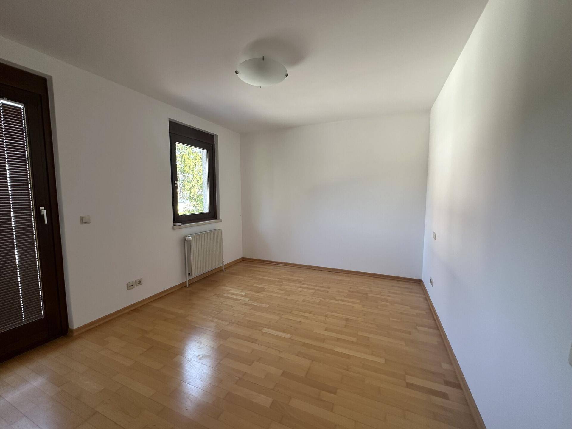 Ruhiges Schlafzimmer mit Holzboden und Fenster, das viel Tageslicht bietet.