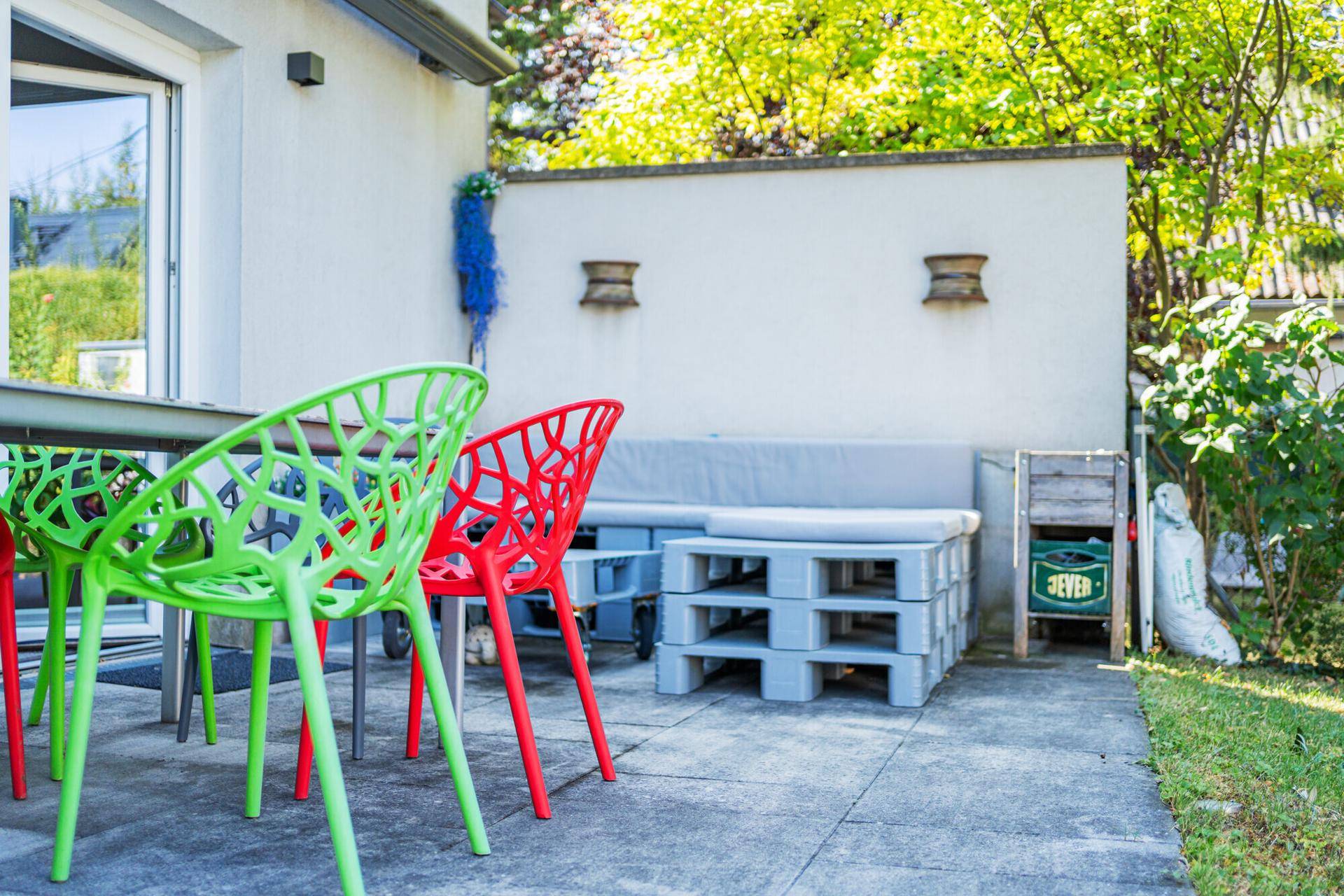 Gemütliche Terrasse mit bunten Stühlen und selbstgebauten Palettenmöbeln im Freien.