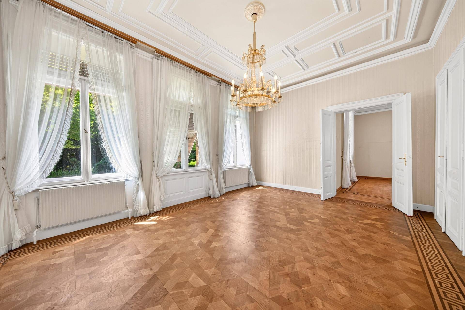 Geräumiges Wohnzimmer mit Fischgrätparkett, hohen Fenstern und Stuckdecke.