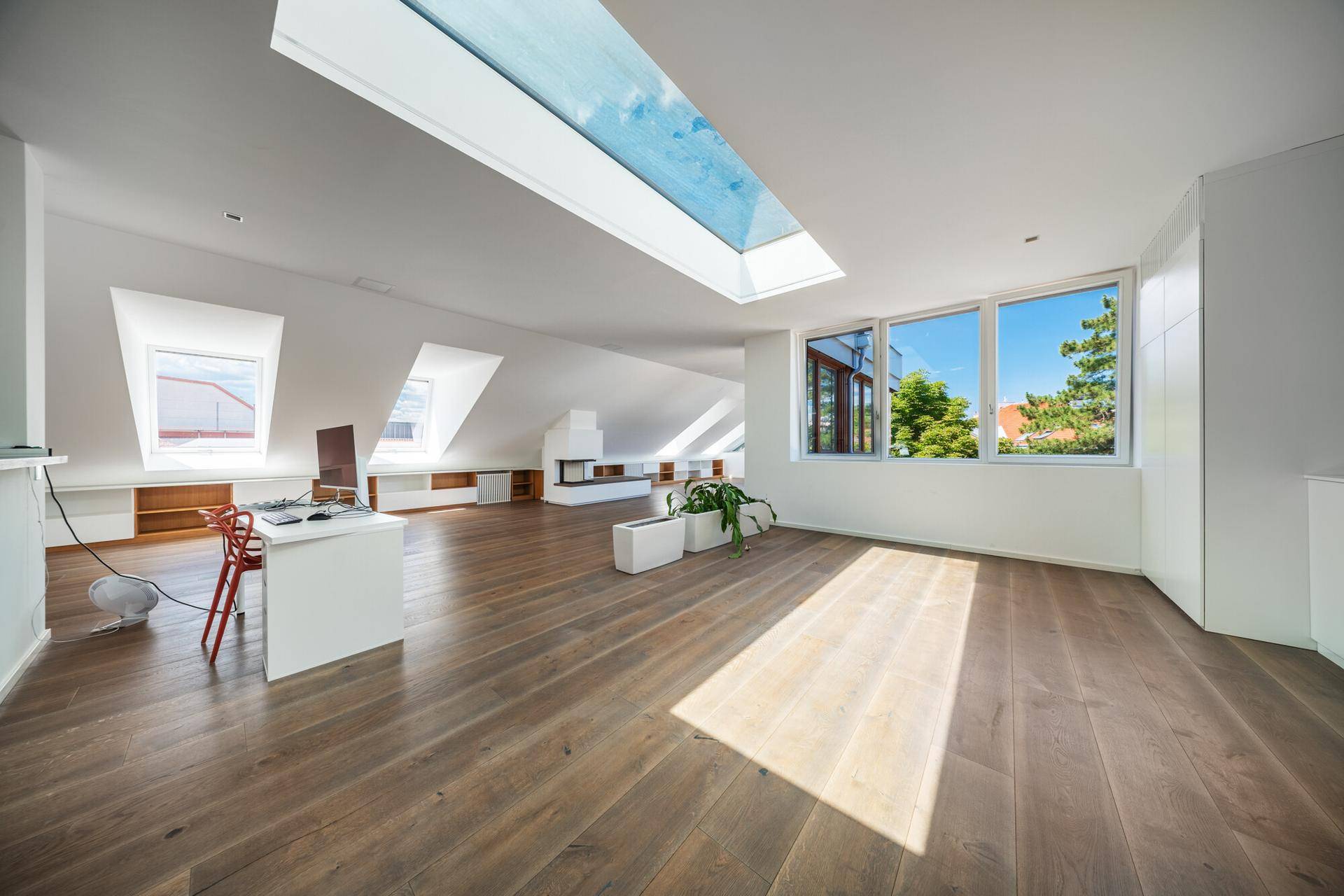 Heller, offener Dachbodenraum mit Holzdielenboden, Oberlicht, schrägen Decken und einem modernen Kamin.